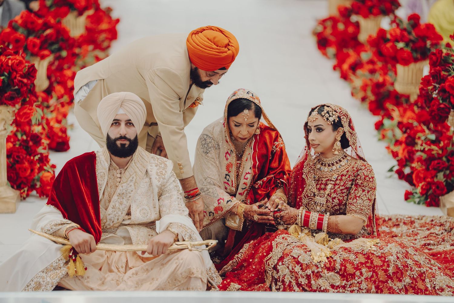 Traditional Sikh wedding ceremony with couple seated among scattered red rose petals and floral decorations.