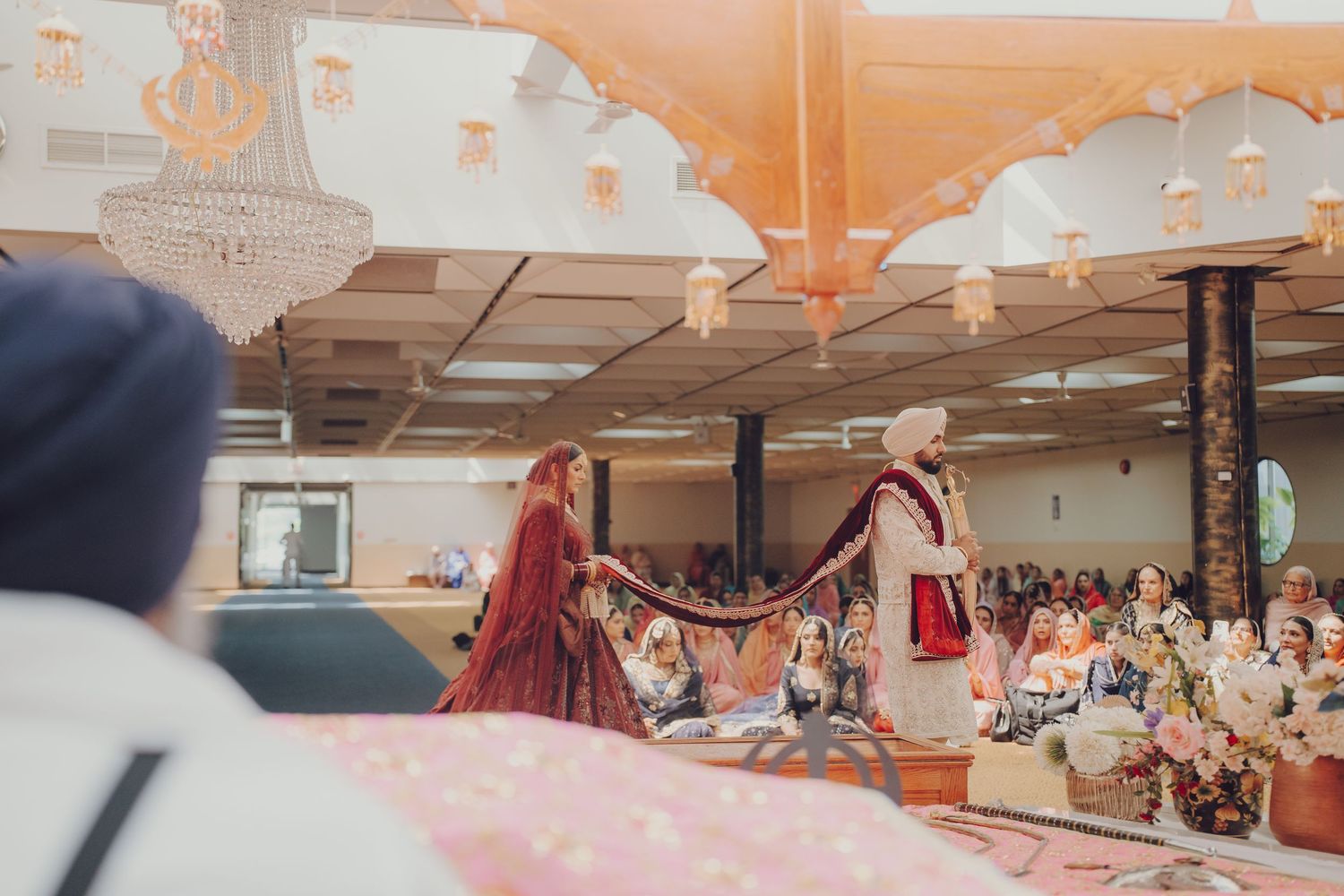 A large indoor wedding reception venue decorated with pink and orange paper lanterns and string lights overhead.