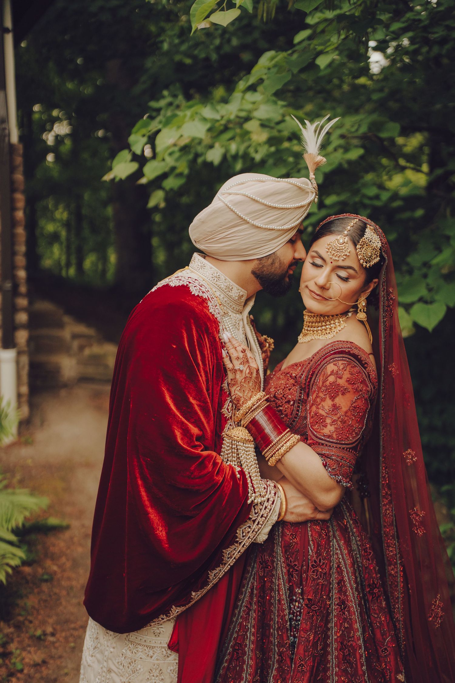 Traditional wedding attire featuring deep red velvet and embroidered details in outdoor garden setting.