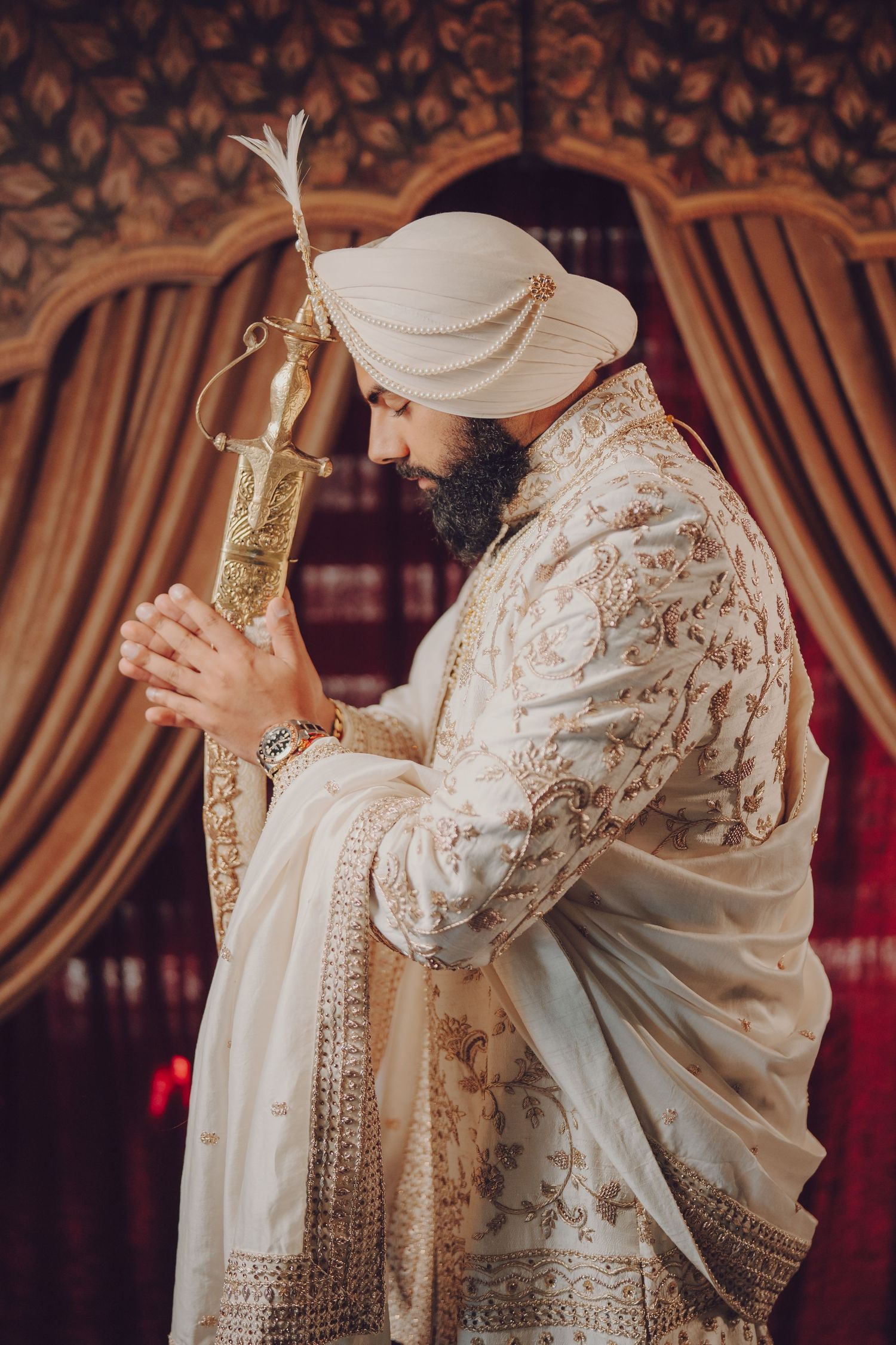 Traditional Indian wedding ceremony with ornate white and gold attire against draped curtains.