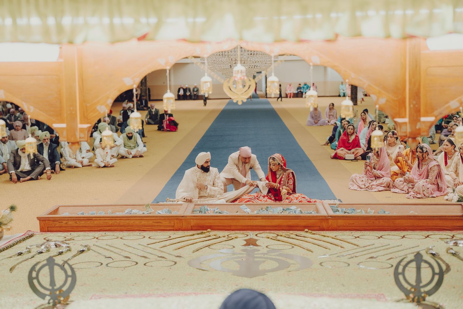 Panoramic view of a Sikh Gurdwara wedding ceremony with guests seated on the floor.