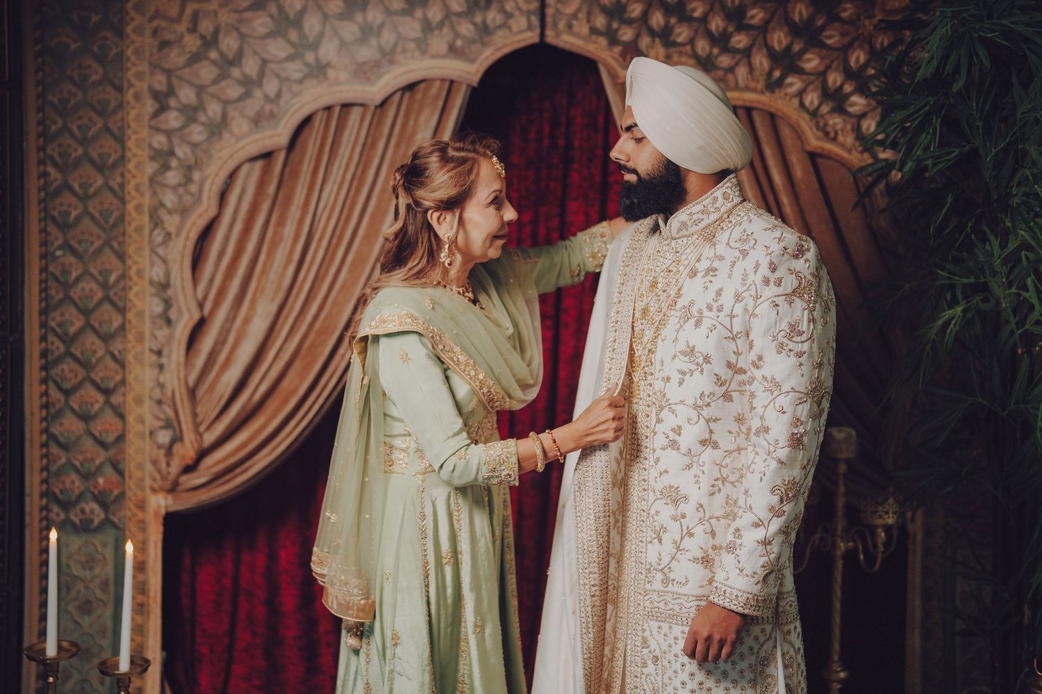 Wedding couple in traditional cream colored outfits standing together under an ornate archway.