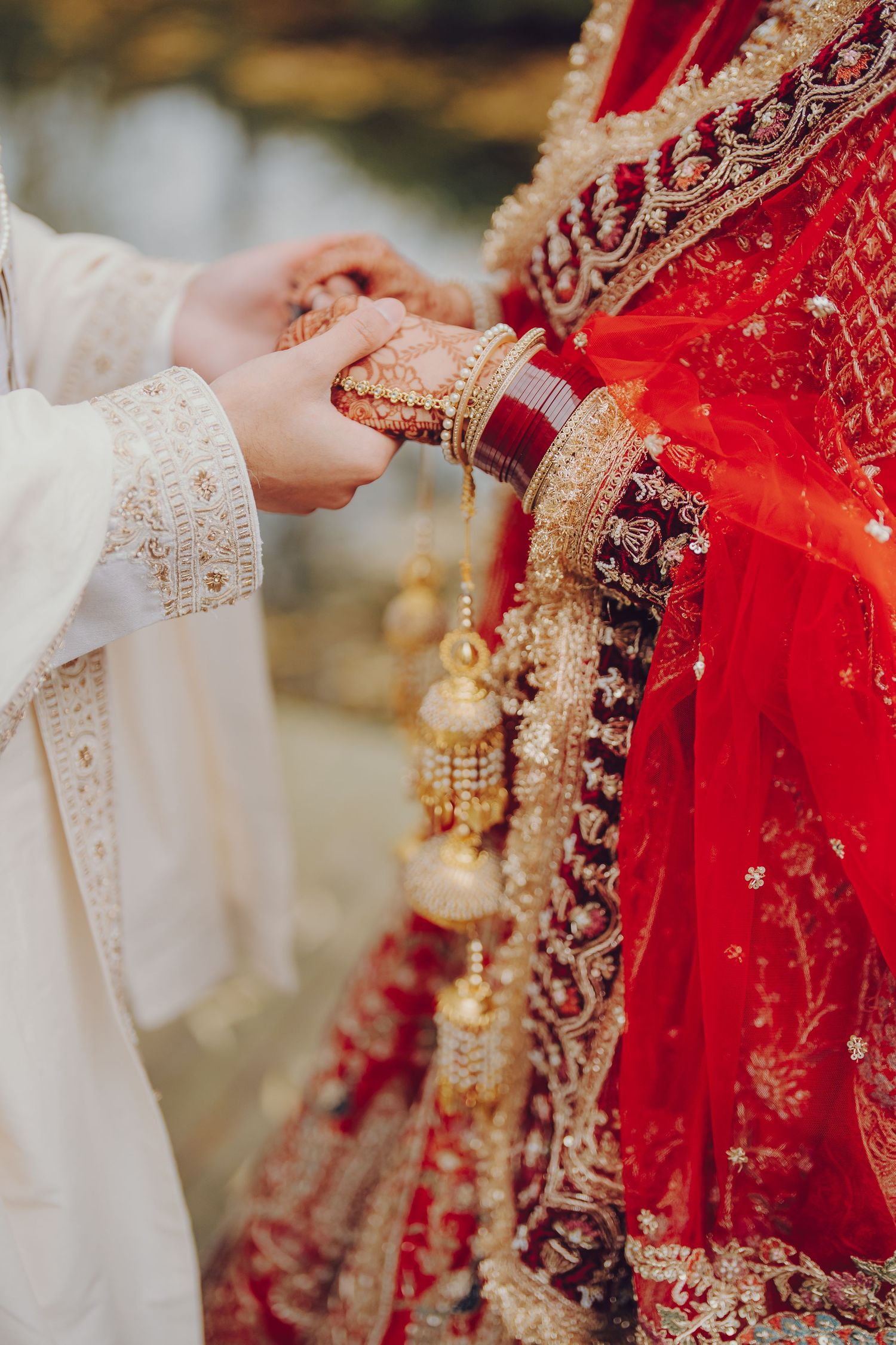 Close-up details of intricate gold jewelry and embellishments on a red bridal lehenga during an Indian wedding ceremony.
