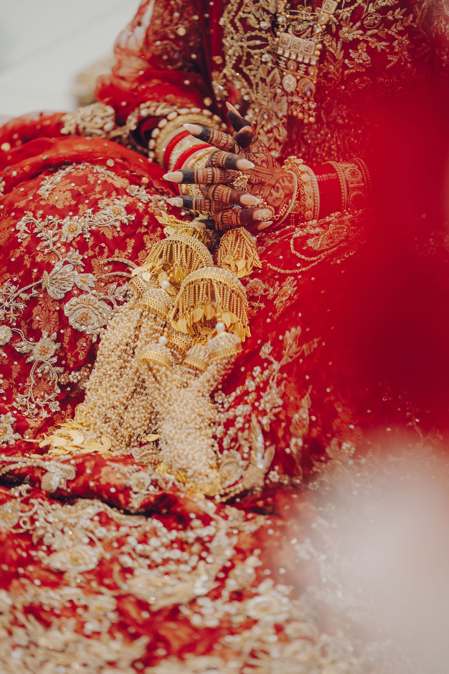 Close-up detail of ornate gold jewelry and henna-decorated hands against a rich red background at an Indian wedding ceremony.