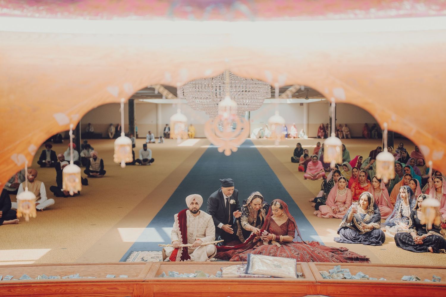 Wide panoramic view of guests seated on the floor during a traditional Sikh wedding ceremony.