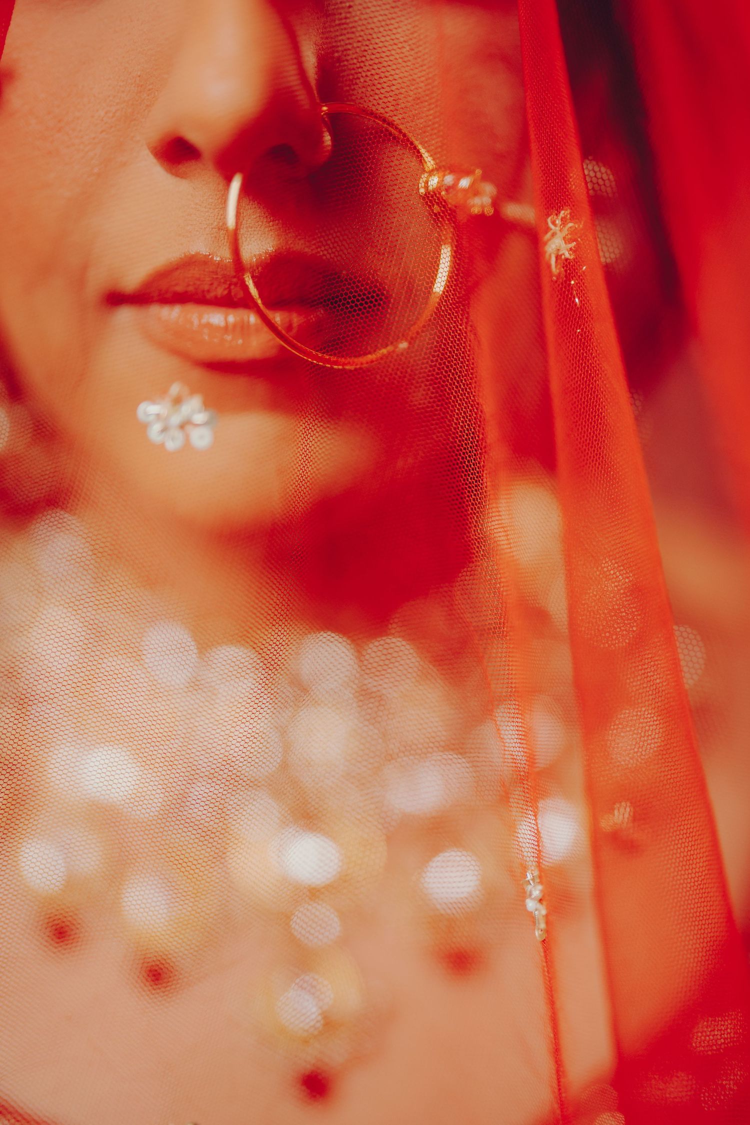 Soft focus portrait through red veil with sparkling jewelry details.