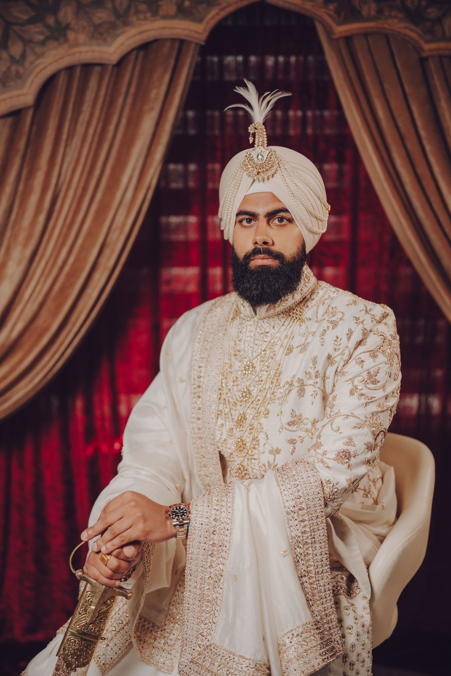 Sikh groom in elegant ivory sherwani with gold embellishments seated during wedding ceremony.