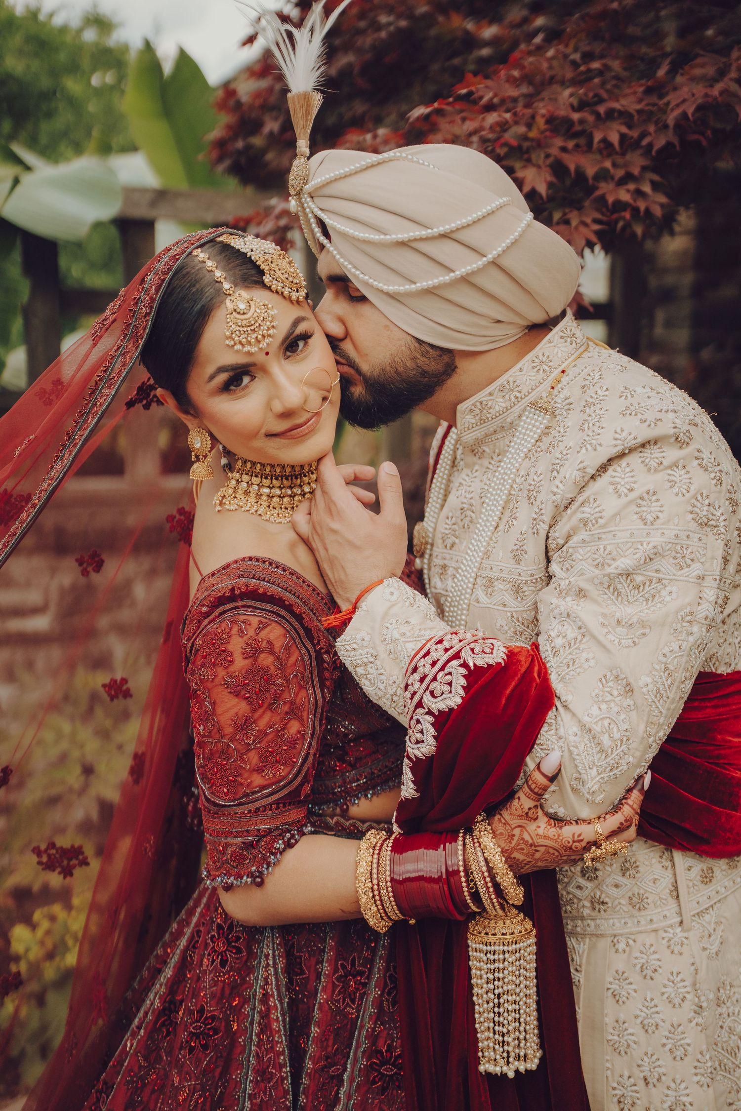 Romantic couple in traditional Indian wedding attire embracing outdoors among autumn foliage.