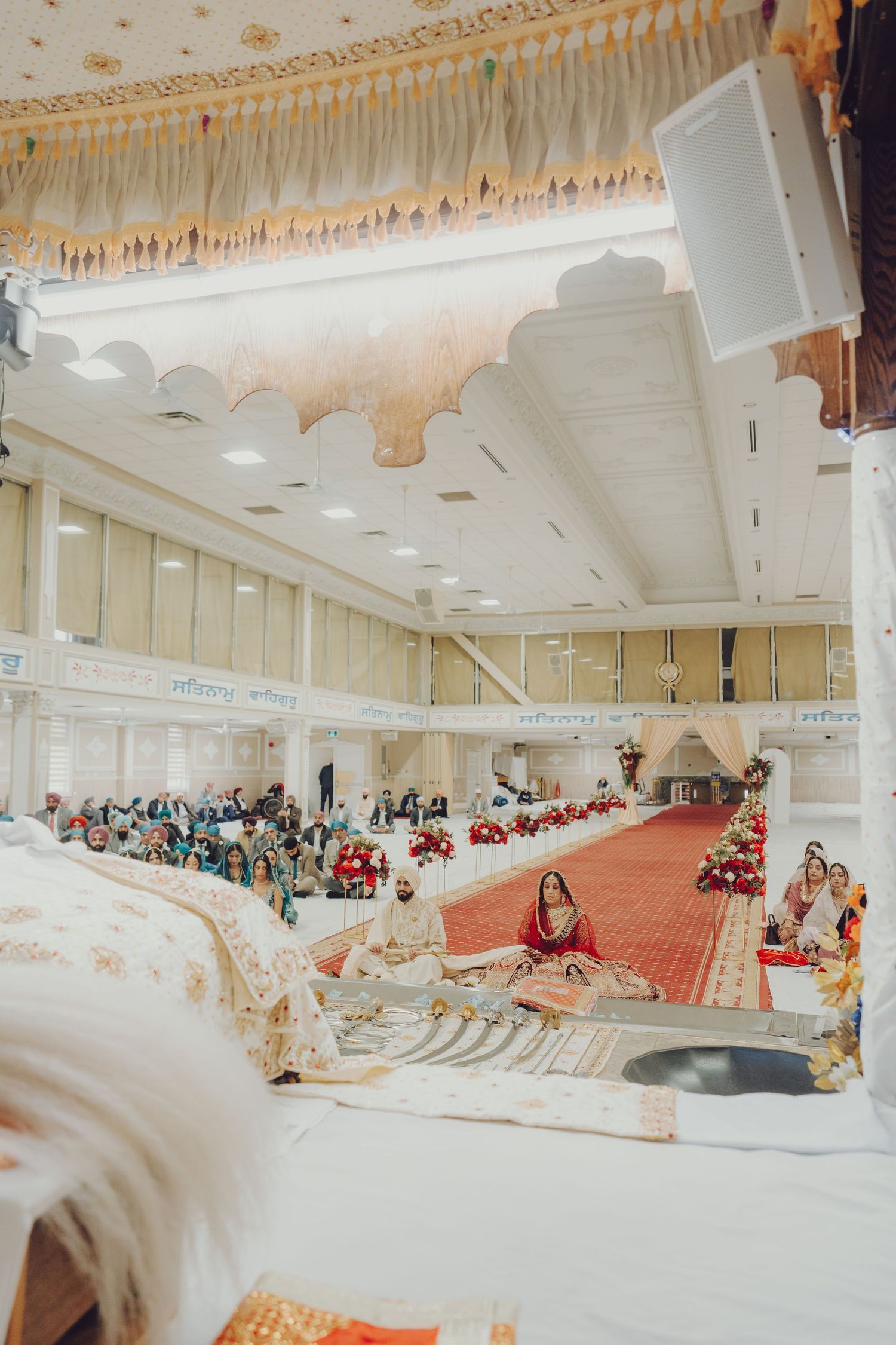 Wide view of an elegant wedding hall with white decor and guests seated for a traditional Indian ceremony.