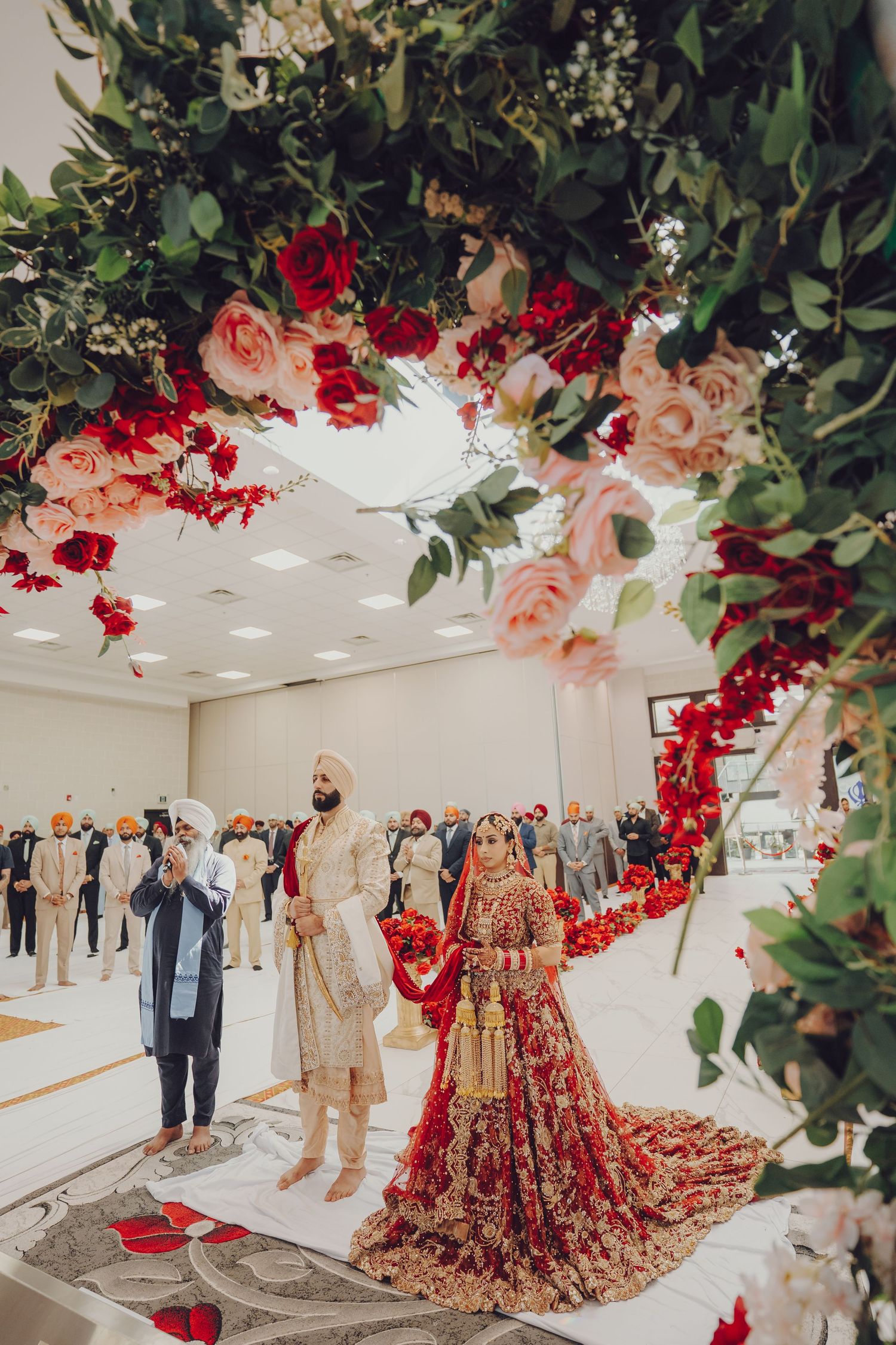 Sikh wedding venue decorated with lush floral garlands featuring red roses and greenery.