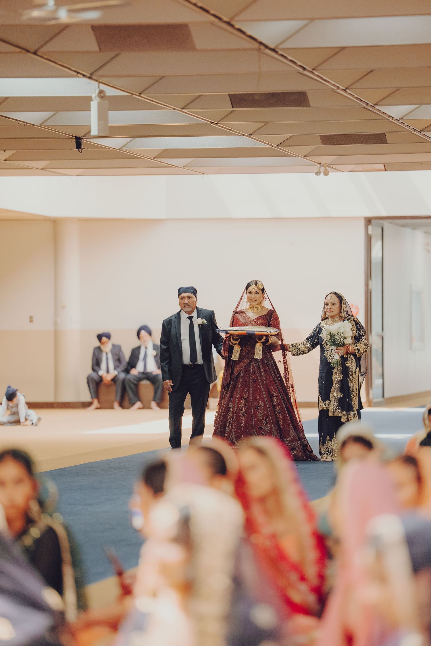 Wedding procession in an indoor venue with guests seated on floor watching the ceremony.