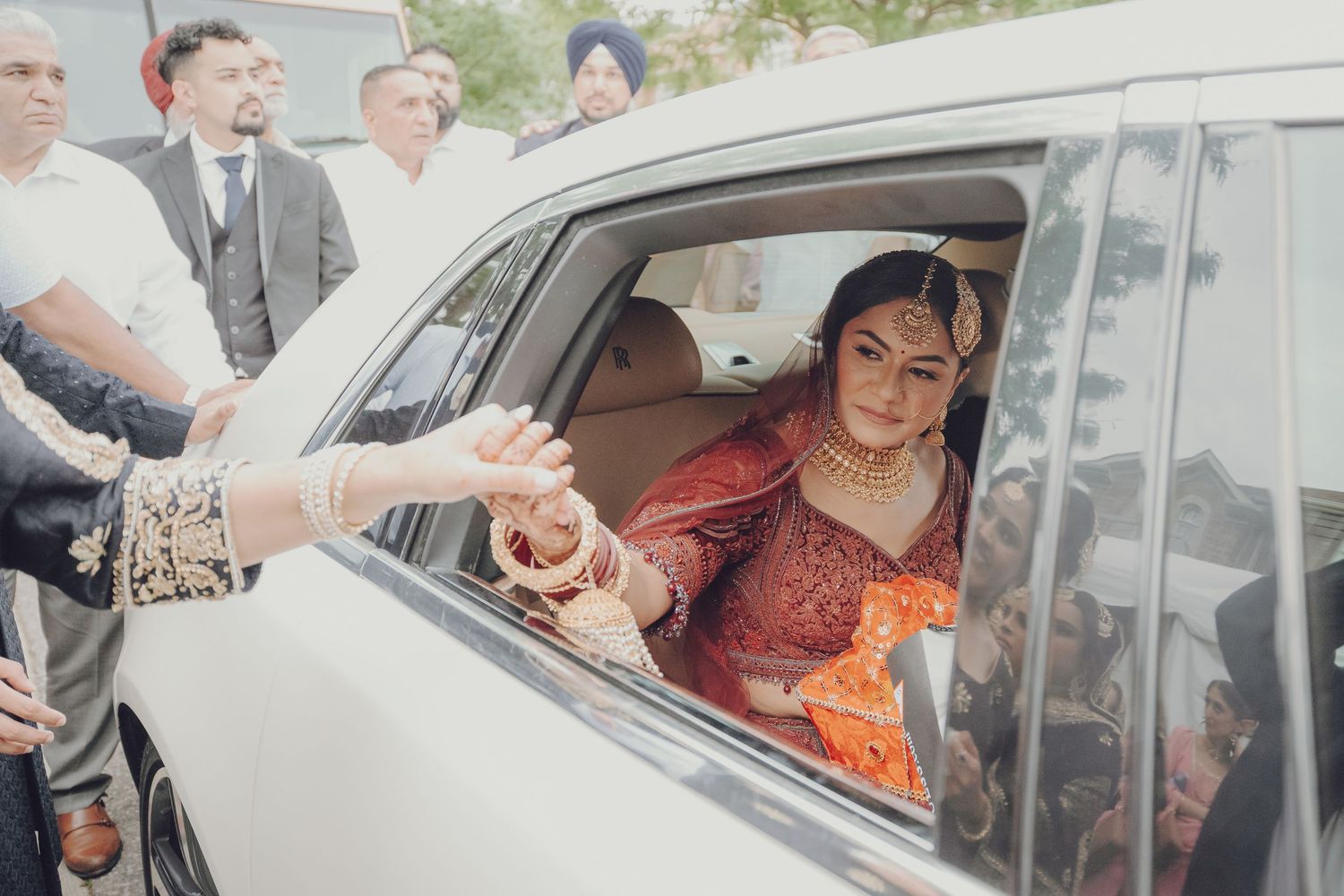 Wedding party gathered around white vehicles during departure ceremony with traditional decorations.