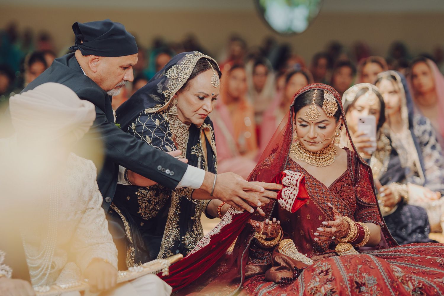 Bride in traditional red Indian wedding attire receives blessings during a cultural ceremony.