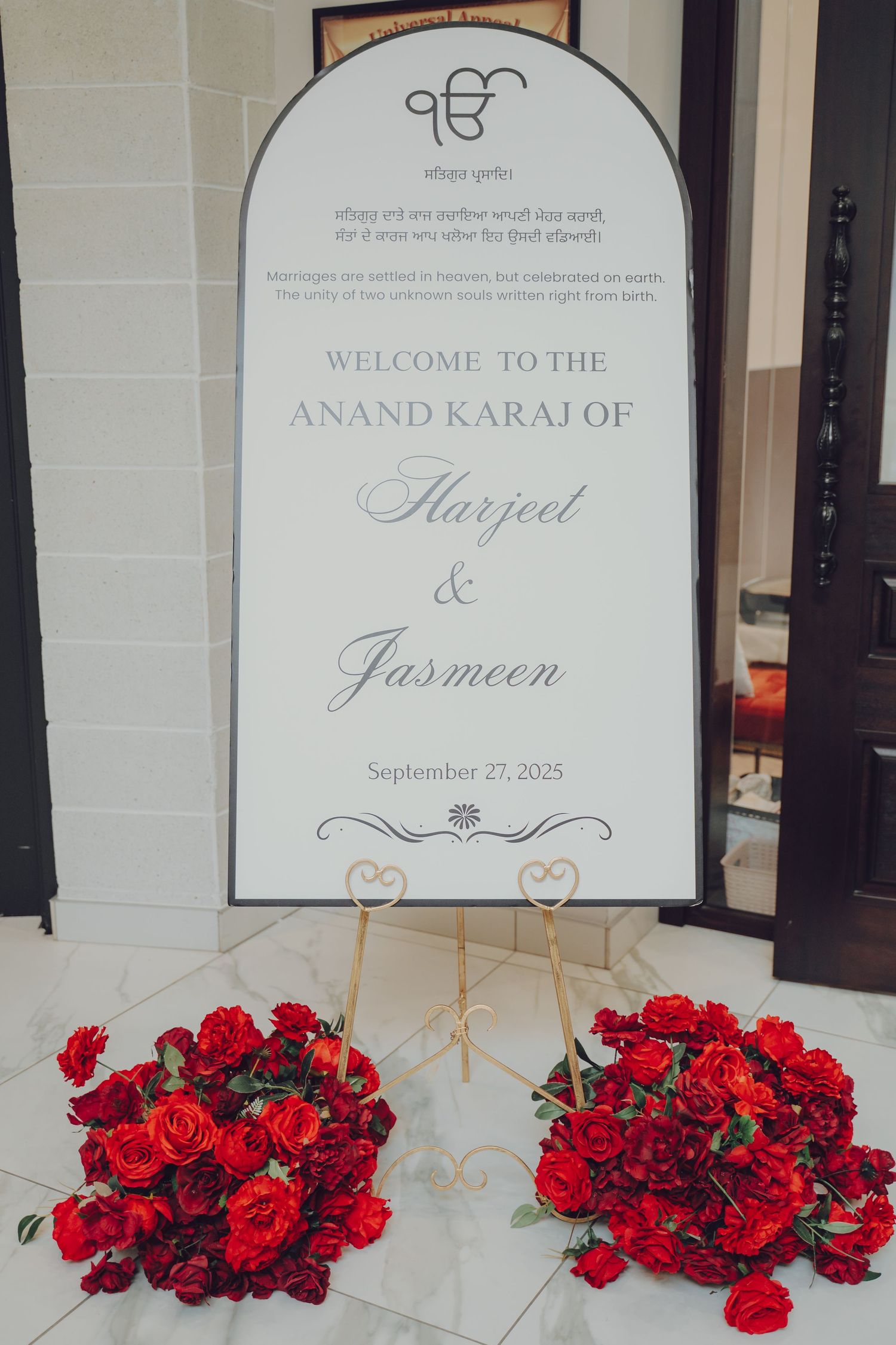 Wedding welcome signs with red rose arrangements displayed on white pedestals at a Sikh ceremony entrance.
