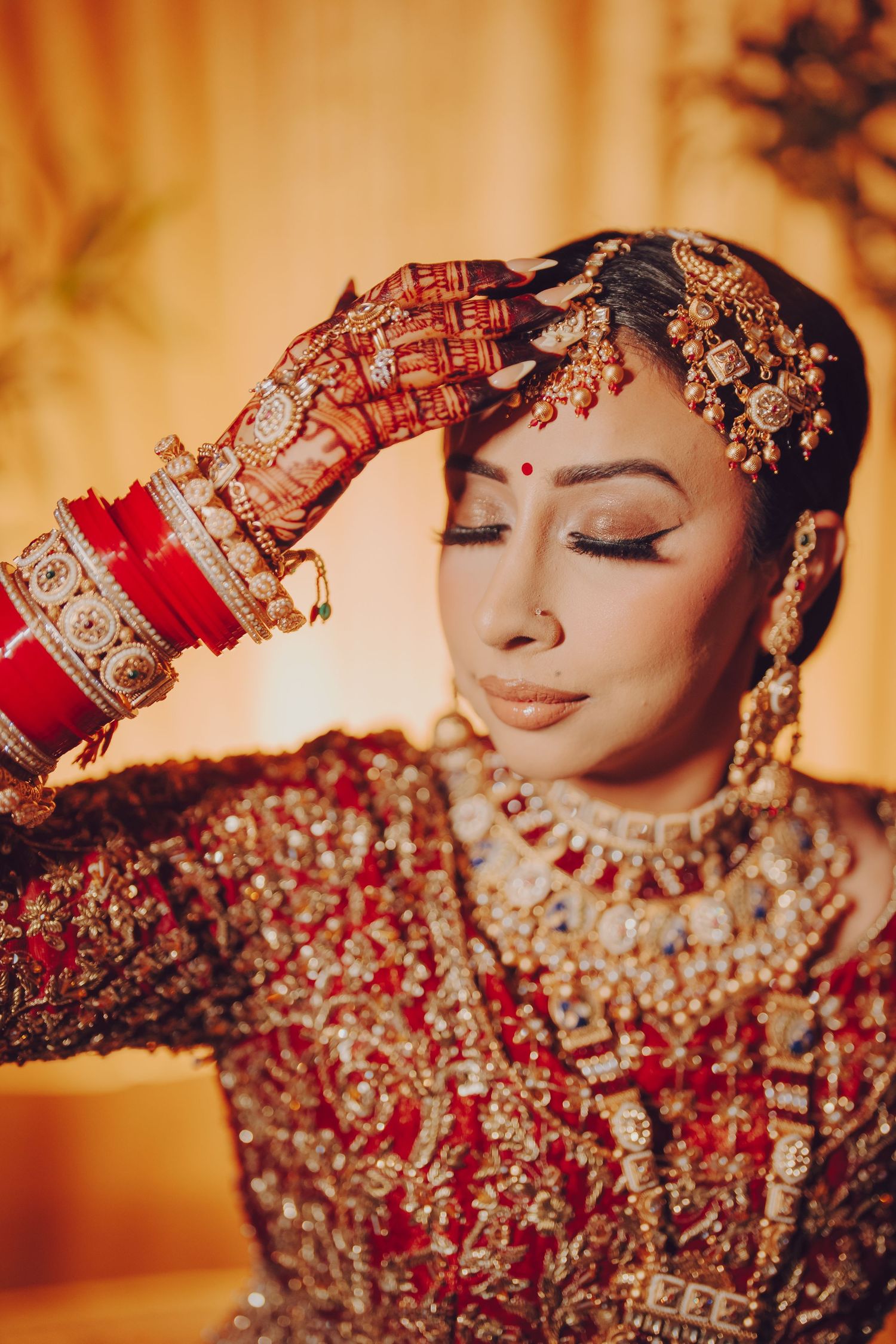 Ornate bridal jewelry and henna adorns hands in traditional South Asian wedding attire.