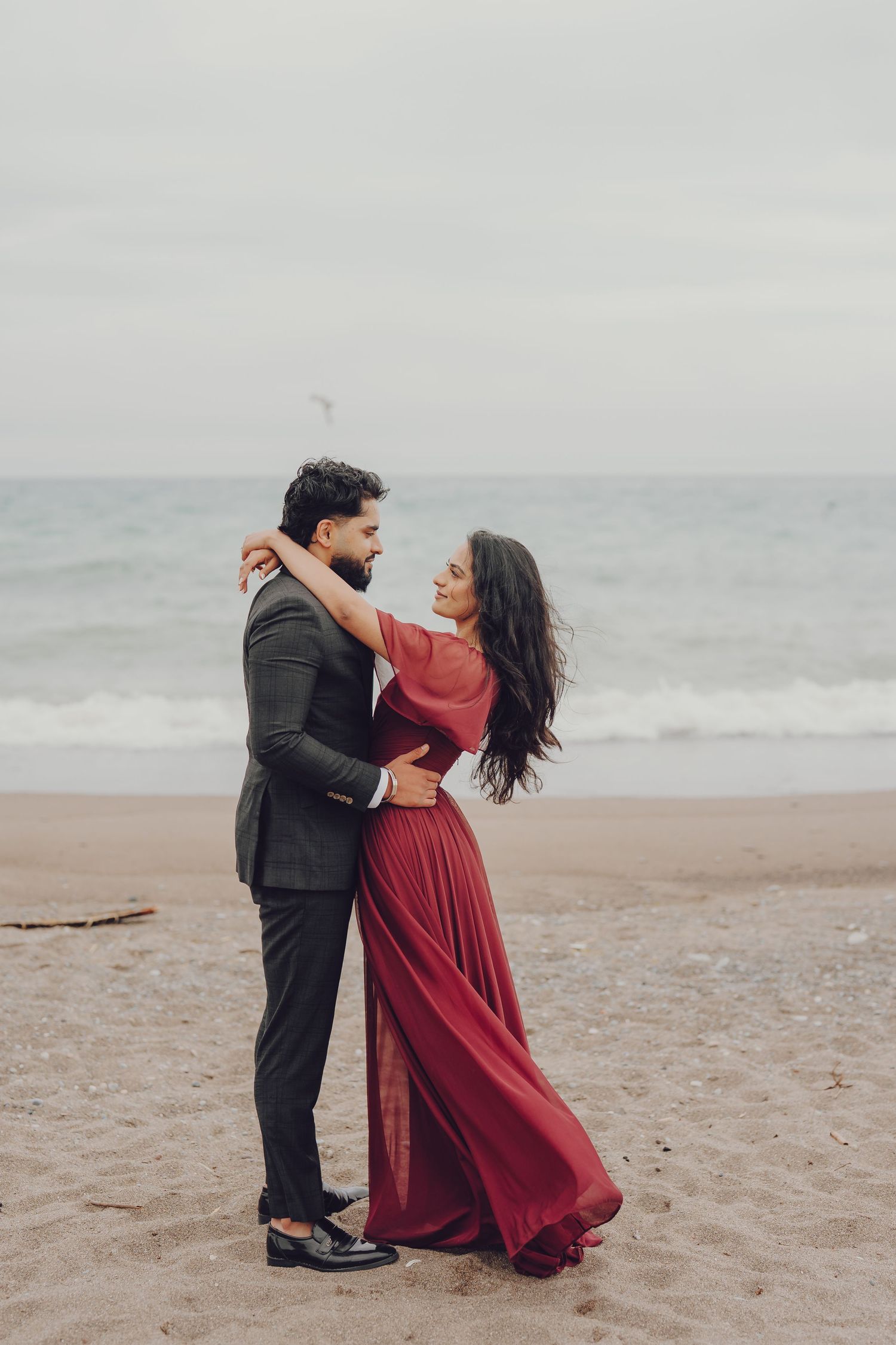 Romantic couple dancing on a misty beach with the woman wearing a flowing red dress.