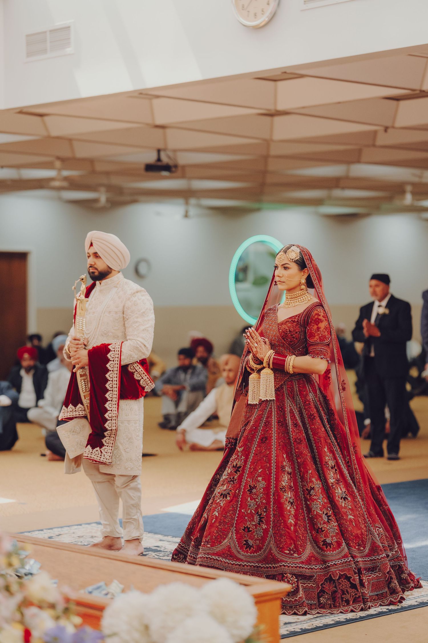 Sikh wedding ceremony in progress showing bride in red lehenga and groom in cream sherwani.
