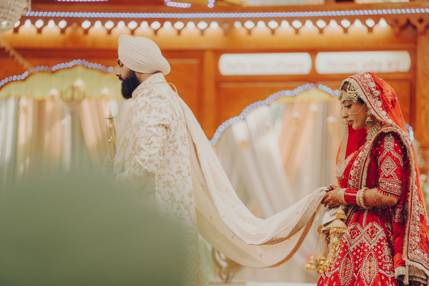 Traditional Sikh wedding ceremony with couple in white and red attire under decorative canopy.