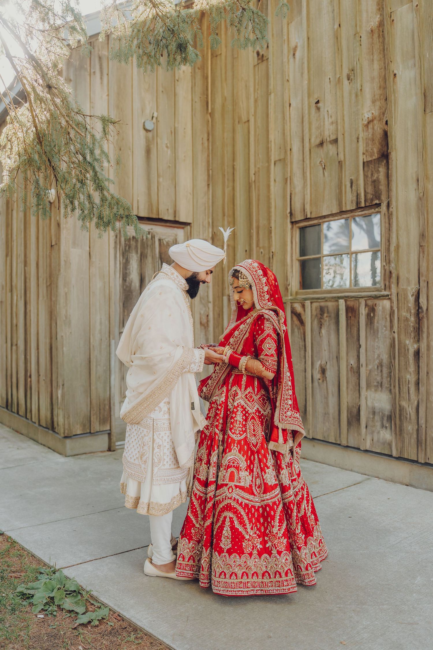 Couple in traditional Sikh wedding attire standing against wooden backdrop during ceremony.