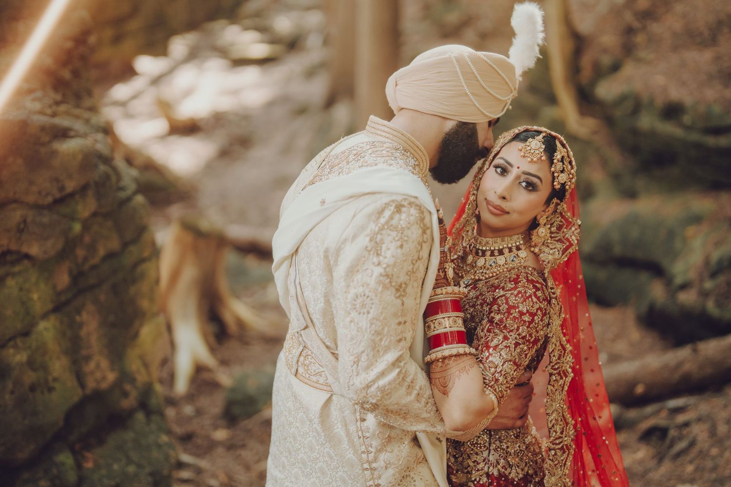 A couple in traditional Indian wedding attire poses together in a lush outdoor garden setting.