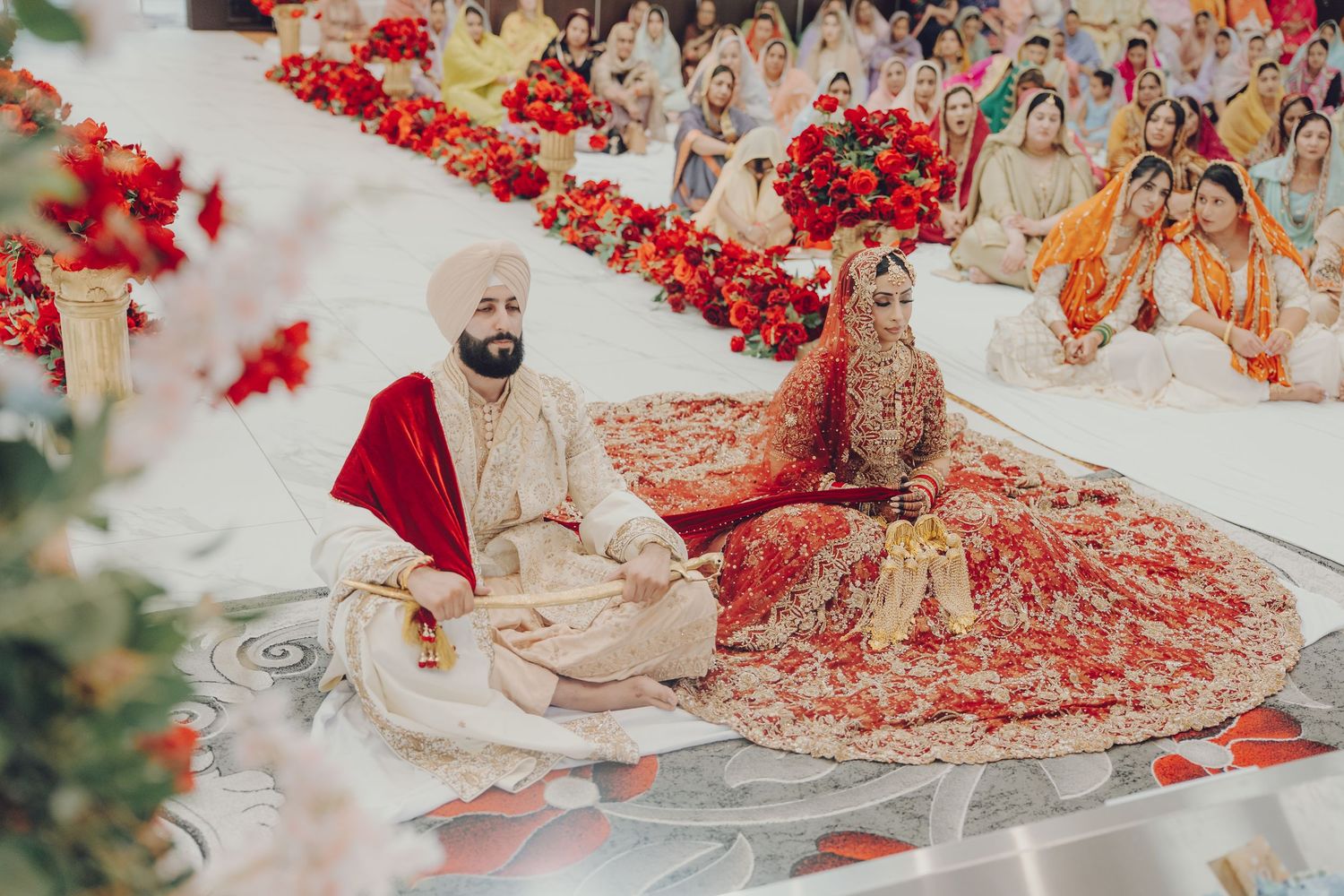 Traditional Indian wedding ceremony with red floral decorations and ornate attire under an elegant mandap setting.