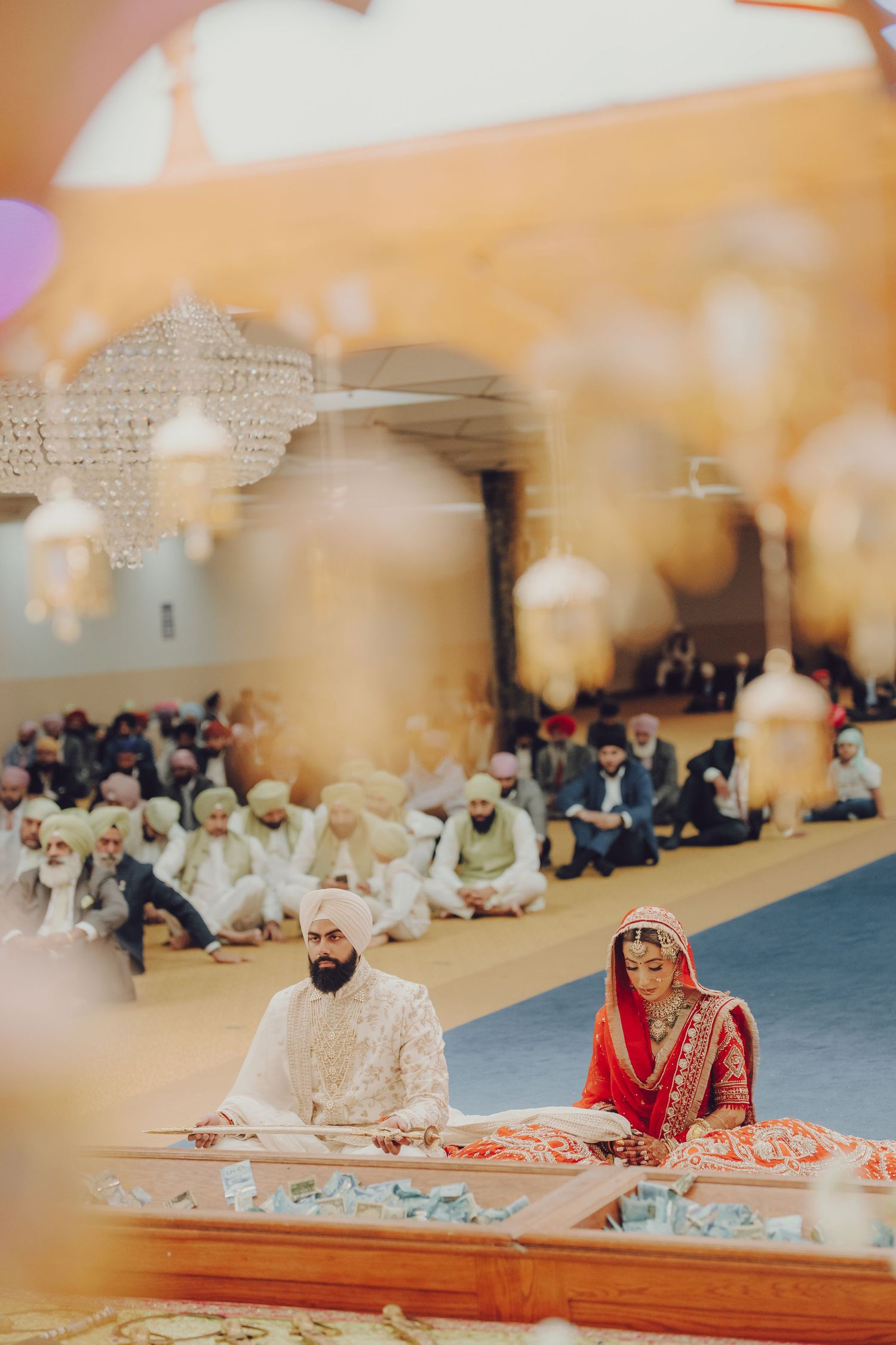 A traditional Sikh wedding ceremony with a couple seated during the Anand Karaj ritual under decorative lighting.