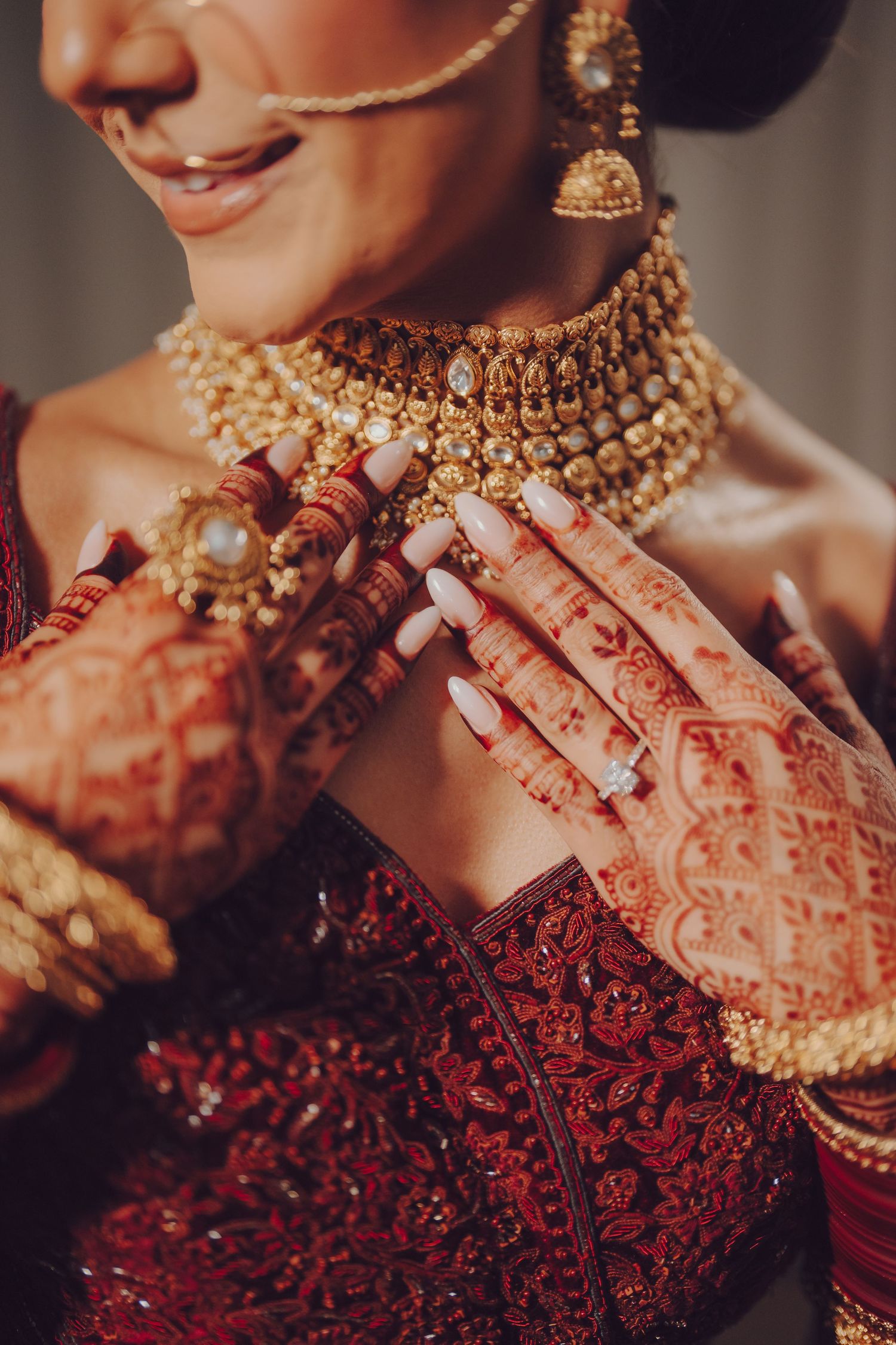 Detailed view of mehndi adorned hands touching an elaborate gold kundan necklace against red bridal wear.