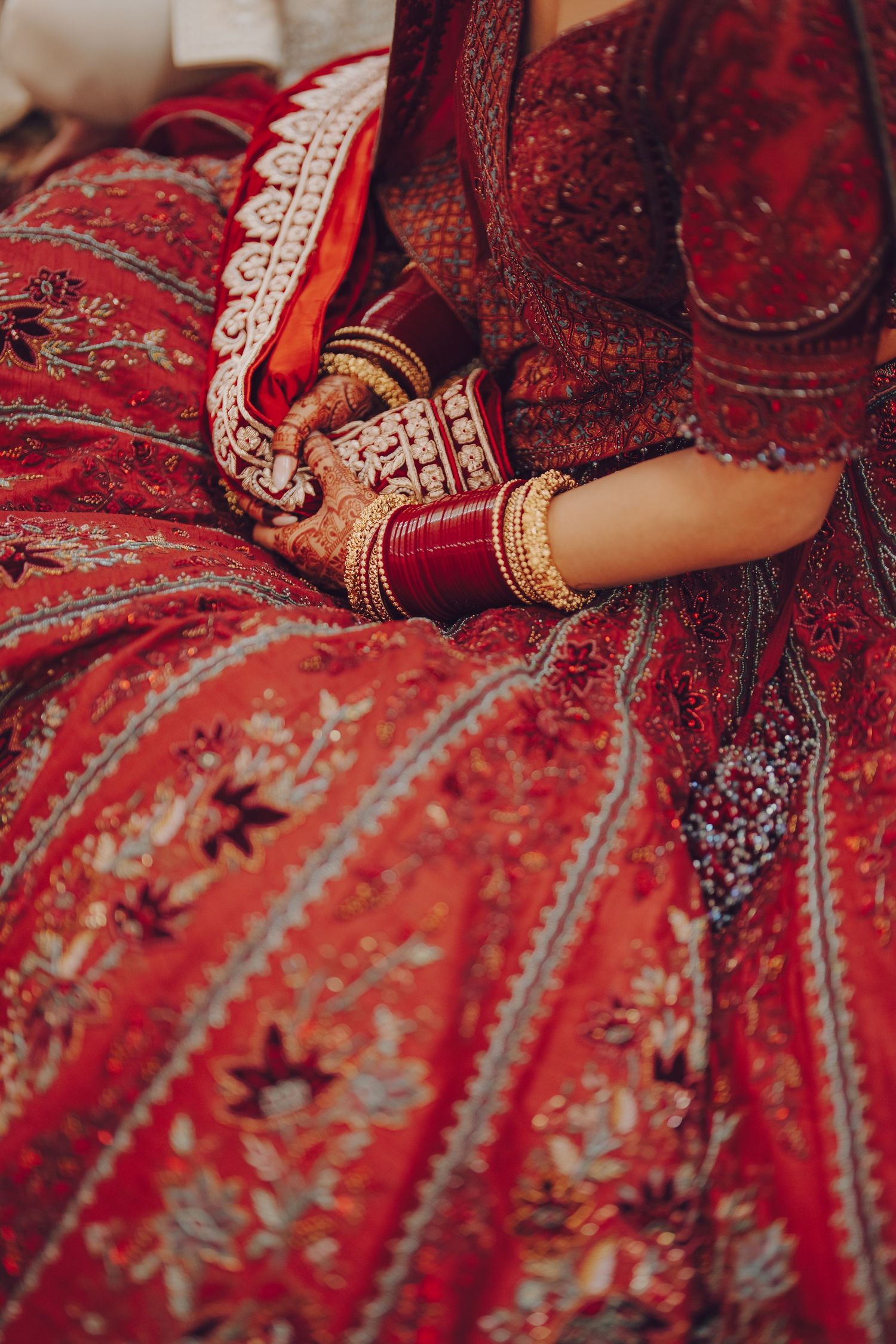 Detailed shot of bridal hands with bangles and mehndi against red embroidered lehenga.