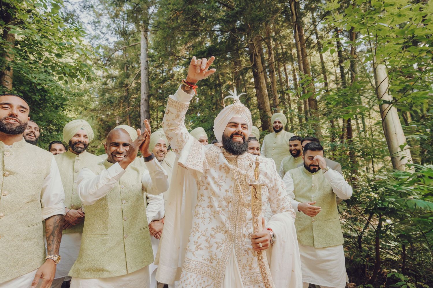 Wedding party celebrating outdoors in light colored attire surrounded by green forest trees.