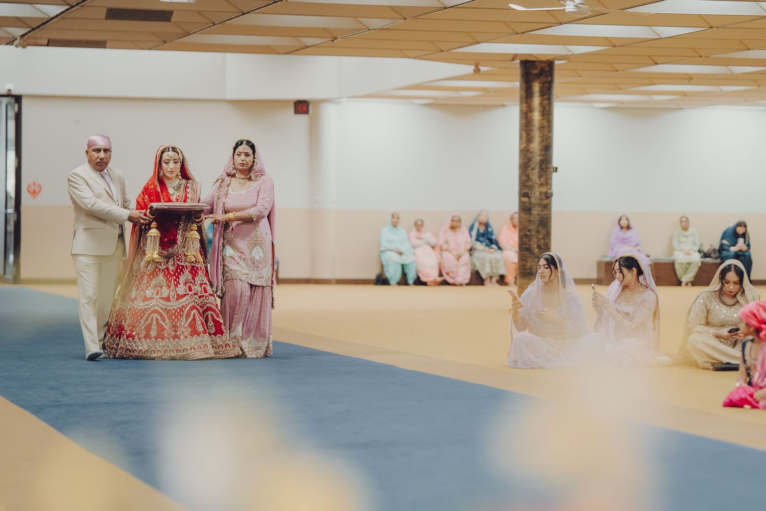 Wide view of a wedding ceremony space with blue carpet and guests in traditional attire.