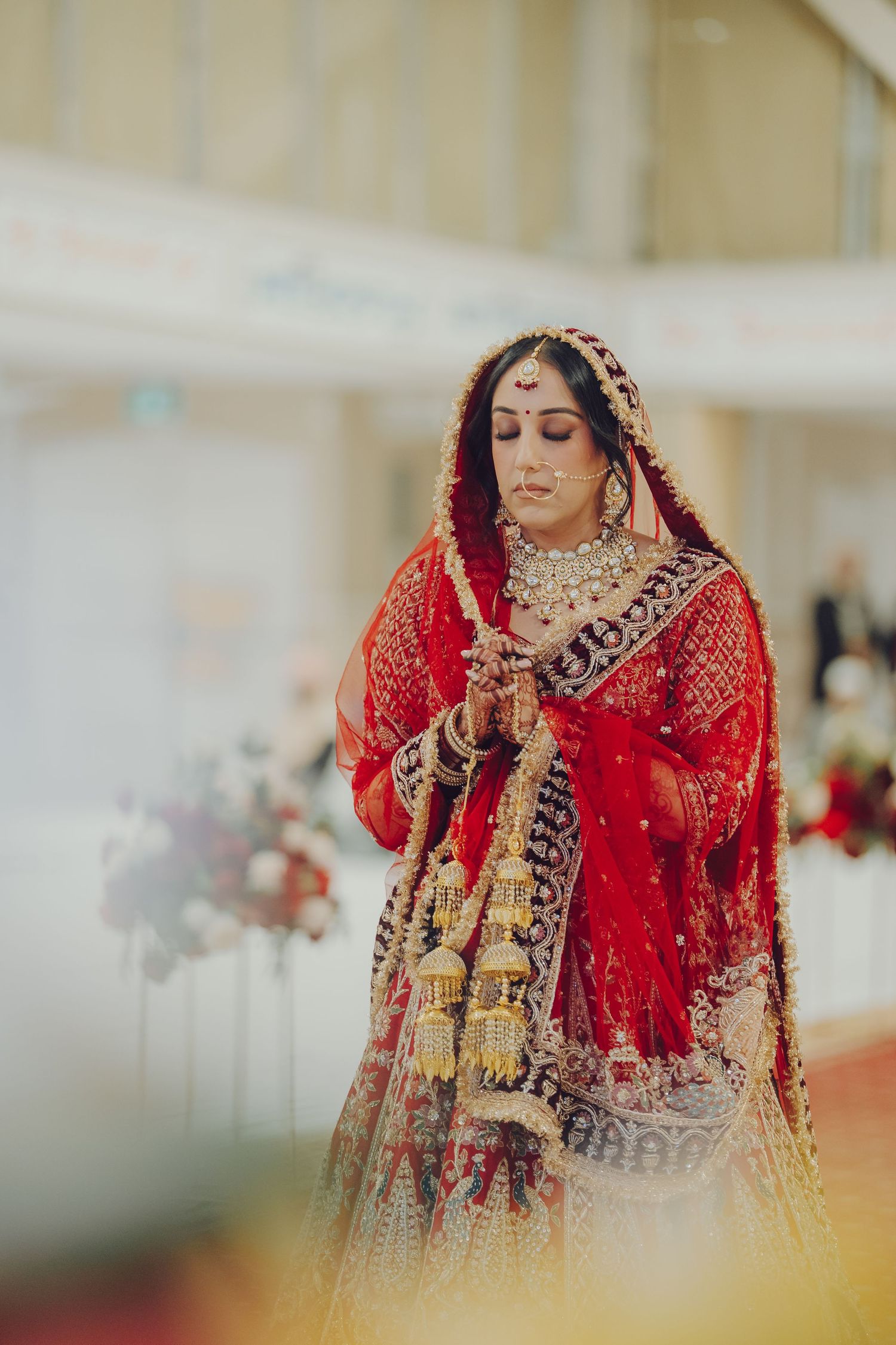 A bride in a stunning red and gold embroidered lehenga during a traditional Indian wedding ceremony.