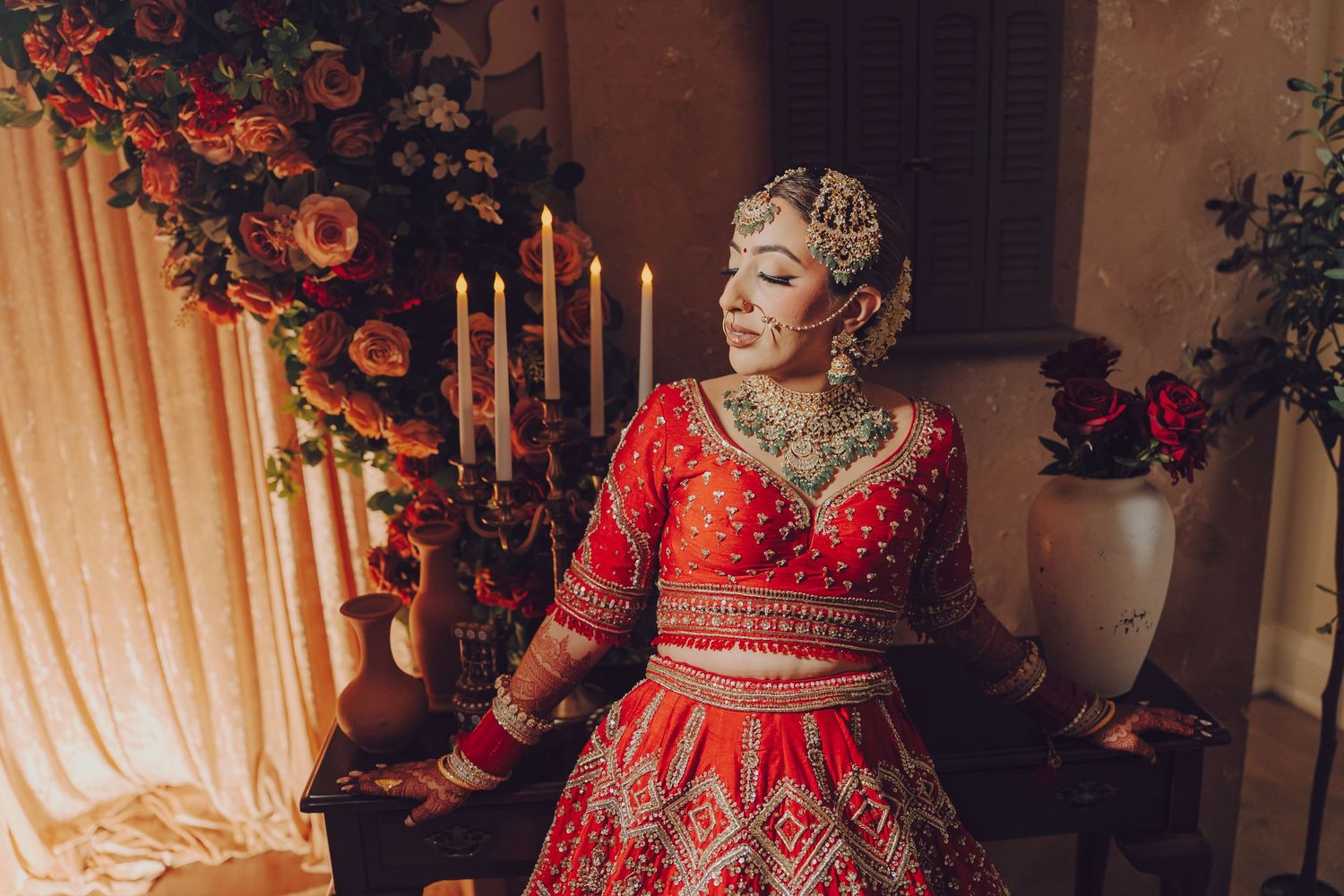 A bride in a stunning red and gold traditional Indian lehenga poses elegantly during a wedding photoshoot.