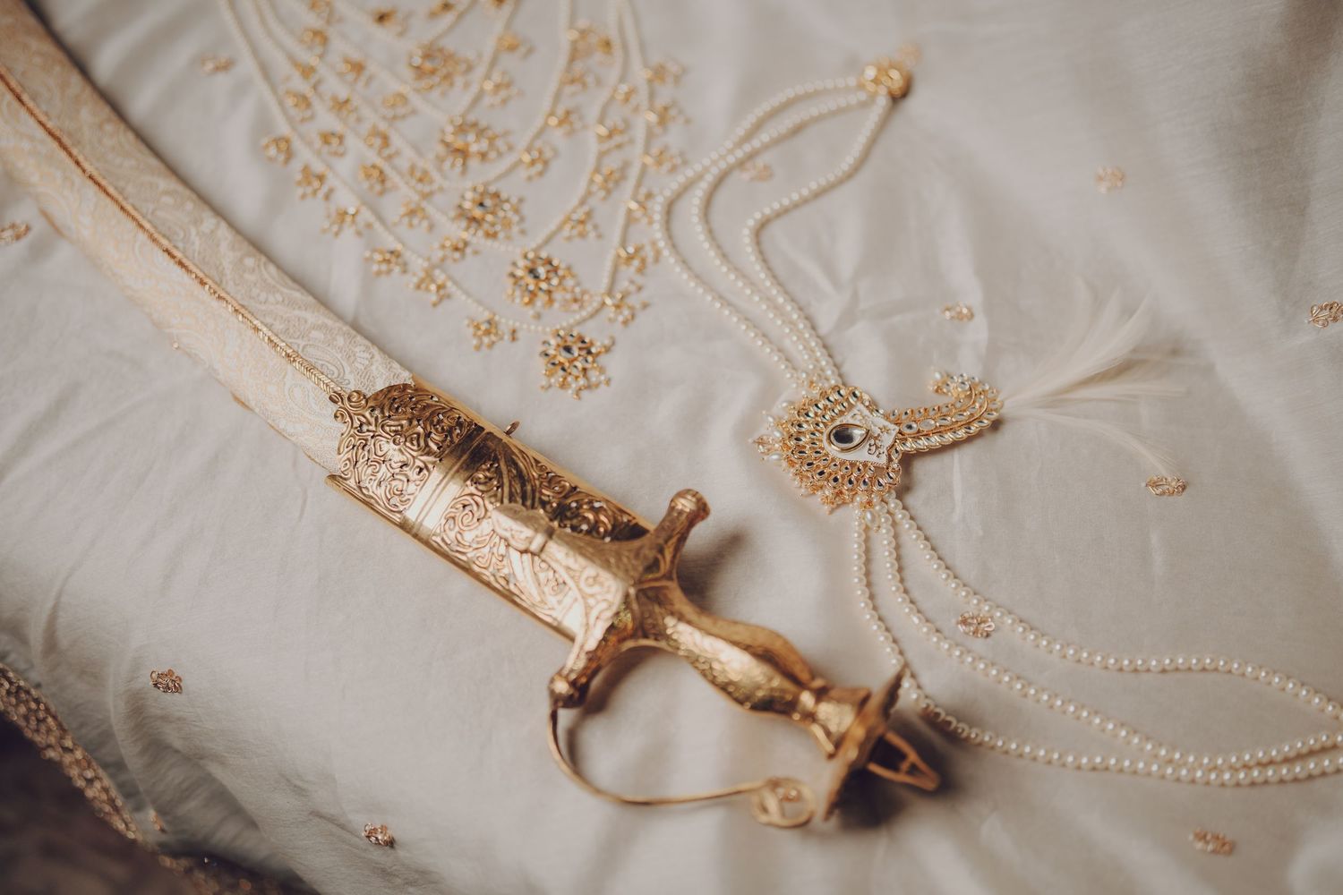 Decorative ceremonial sword with gold details and pearls lying on embroidered white fabric.