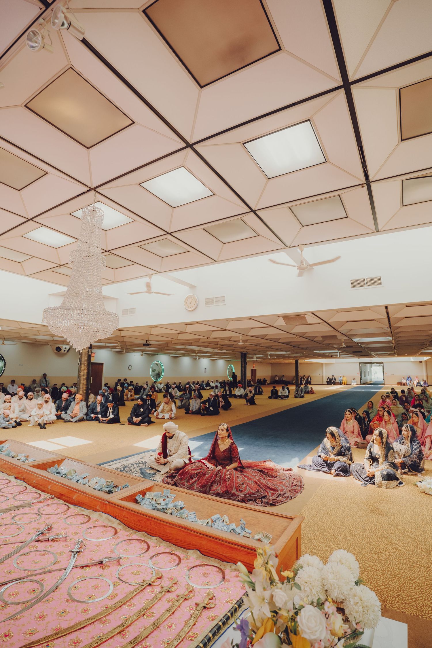Wide angle view of a wedding ceremony in a large hall with guests seated on the floor.