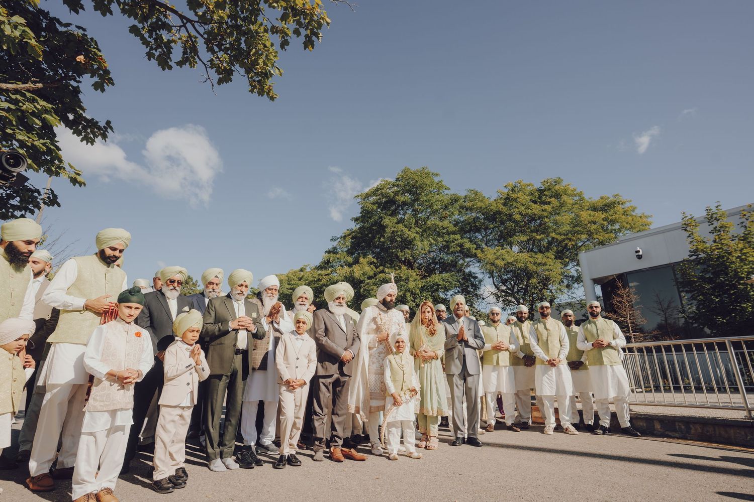 Large group of guests in traditional white attire lined up outdoors during a wedding ceremony.