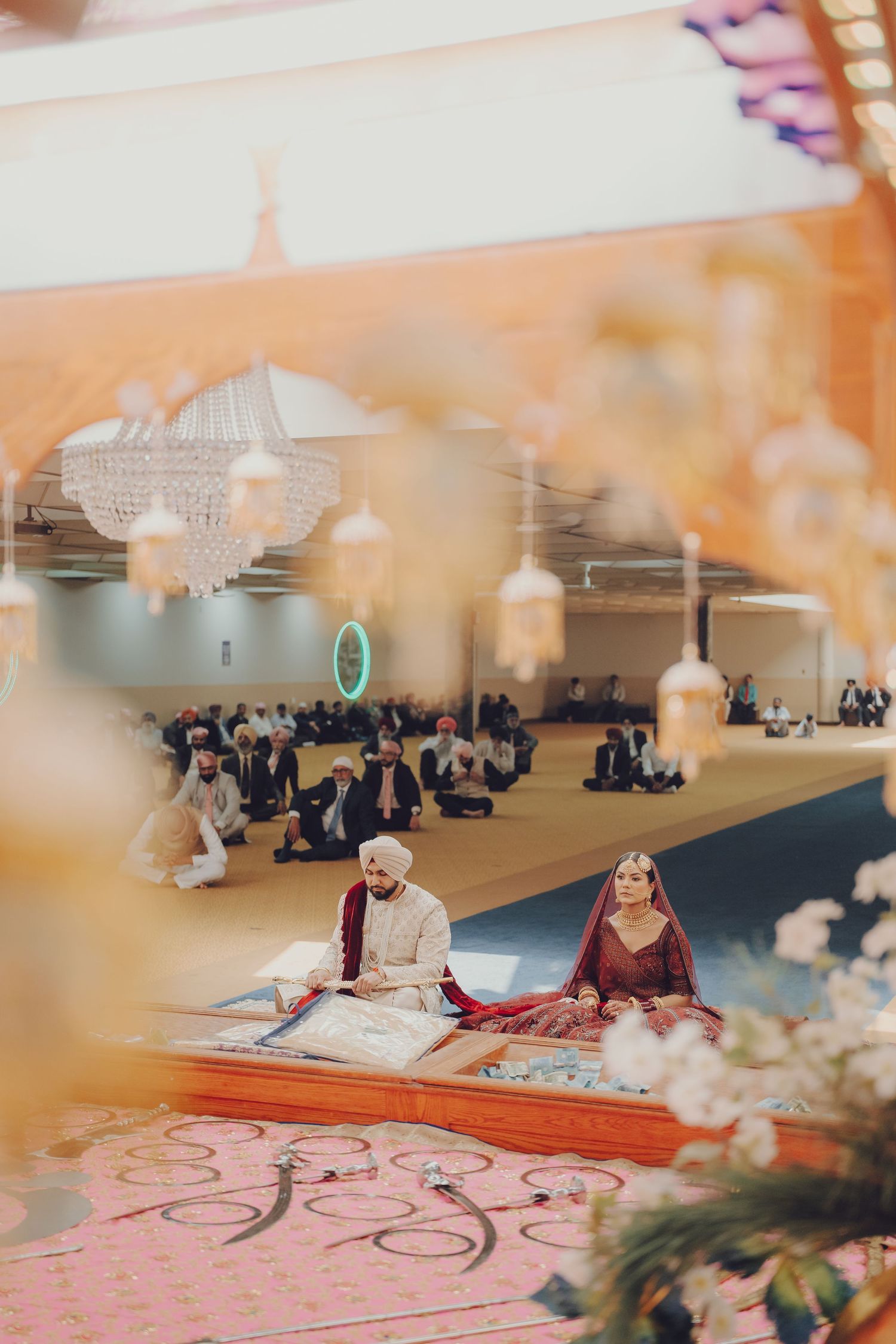 Sikh wedding ceremony taking place in a temple with guests seated on floor mats.