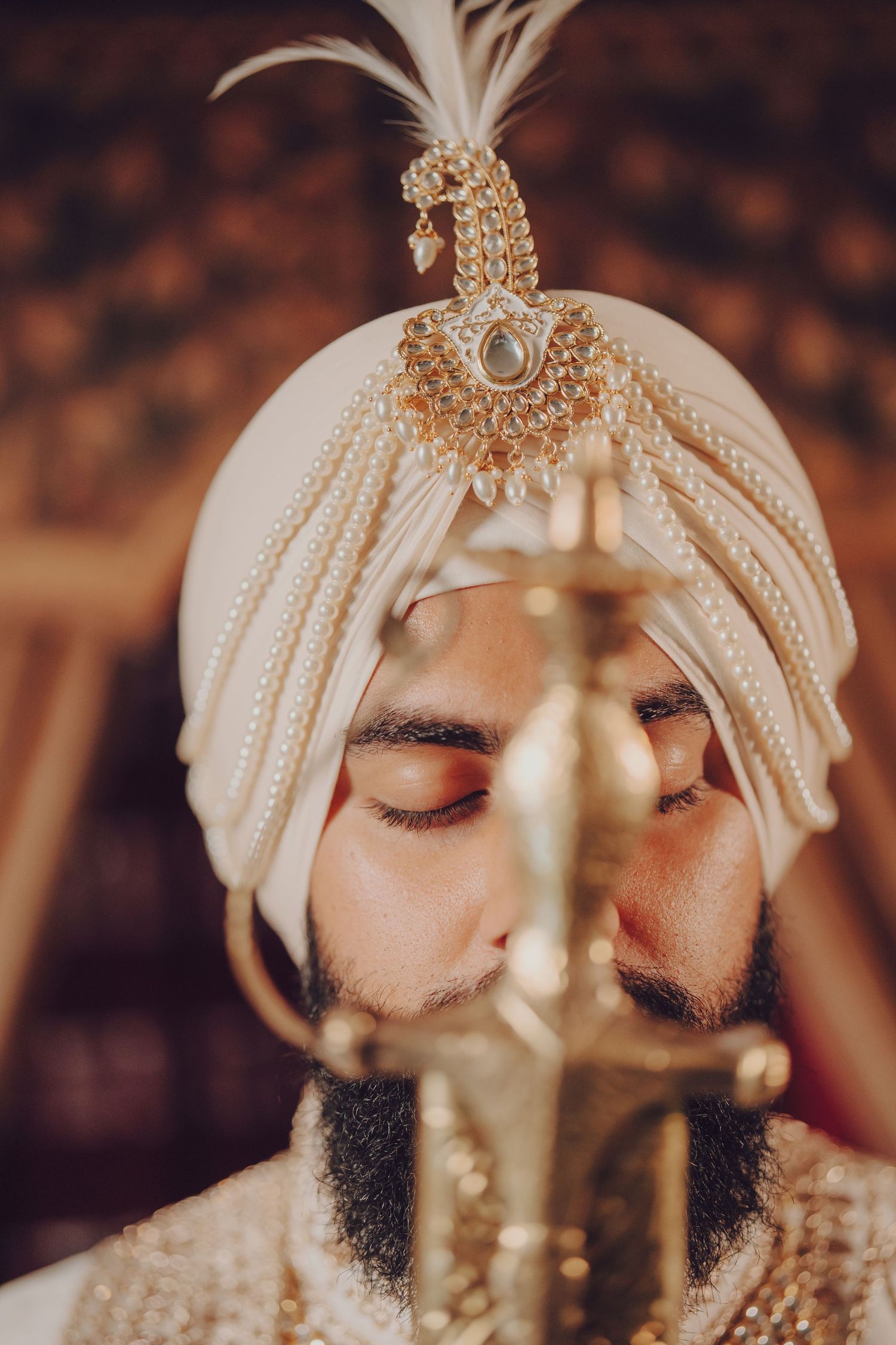 Traditional Sikh groom wearing a cream turban and ornate jewelry during wedding ceremony.
