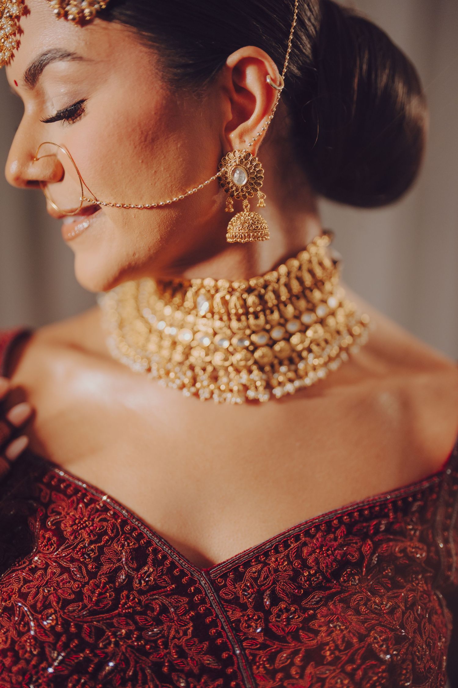 Close-up shot of traditional Indian bridal jewelry featuring an ornate gold choker and jhumka earring with red attire.