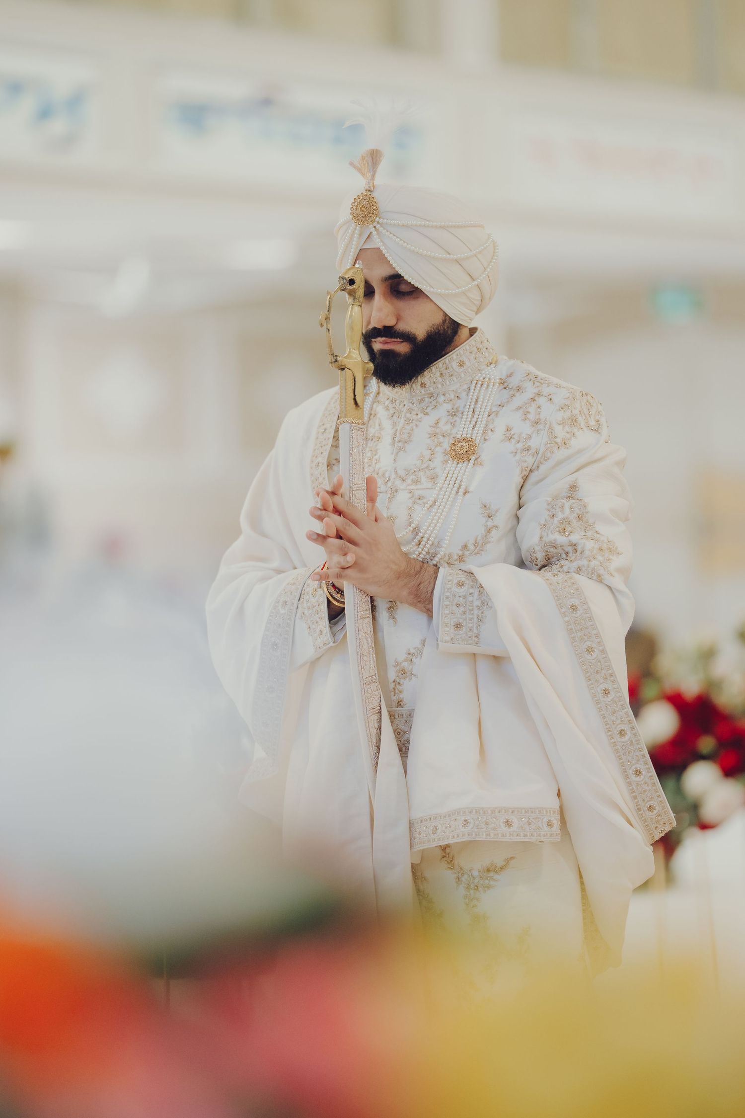 Traditional Sikh ceremony with person in ornate white attire performing rituals.