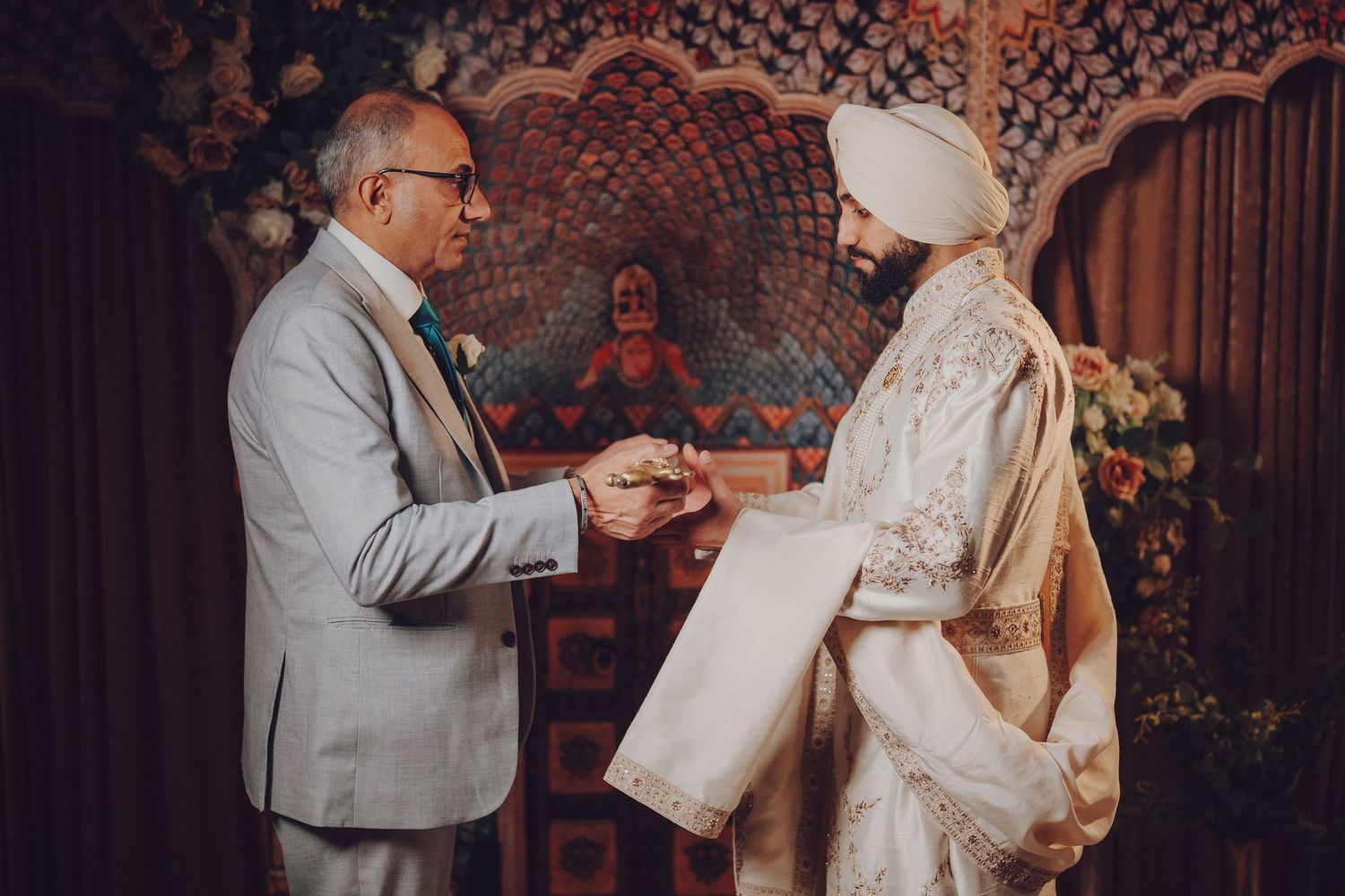 A couple exchanges vows during a wedding ceremony with ornate decor in the background.