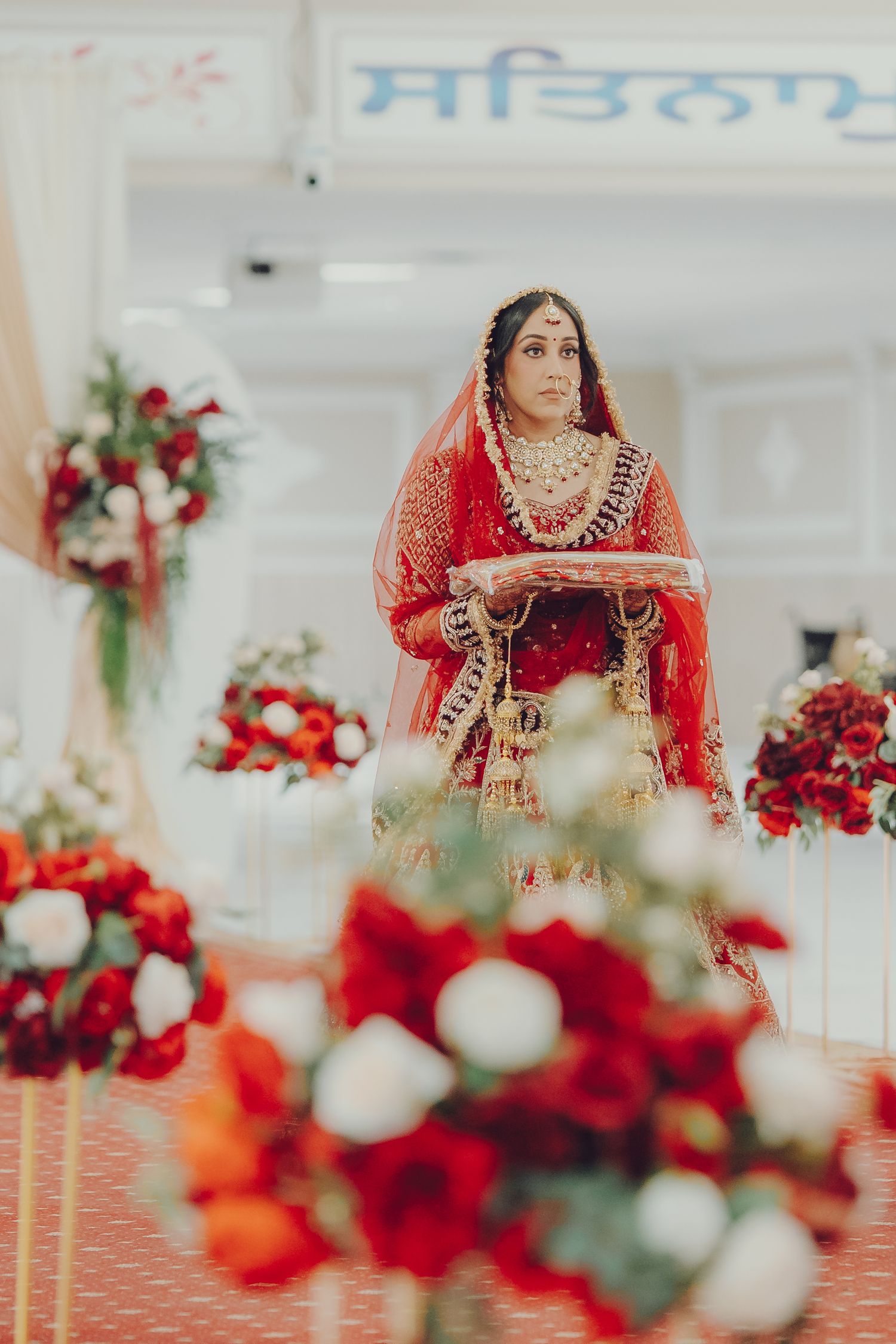 Wedding venue interior with red and white floral centerpieces and traditional Indian decorations.