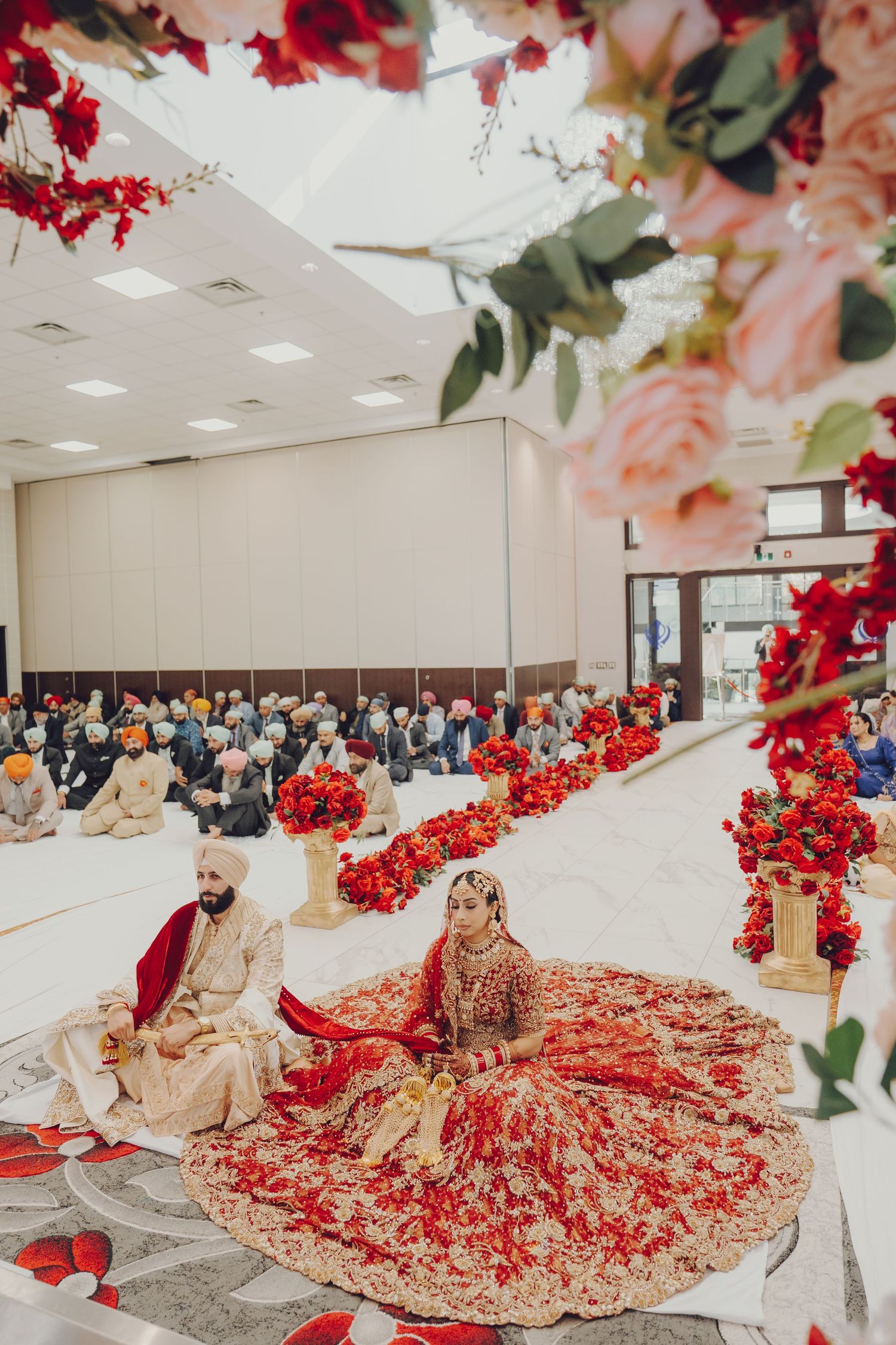 A traditional Indian wedding ceremony decorated with red and pink floral arrangements and elegant bridal attire.