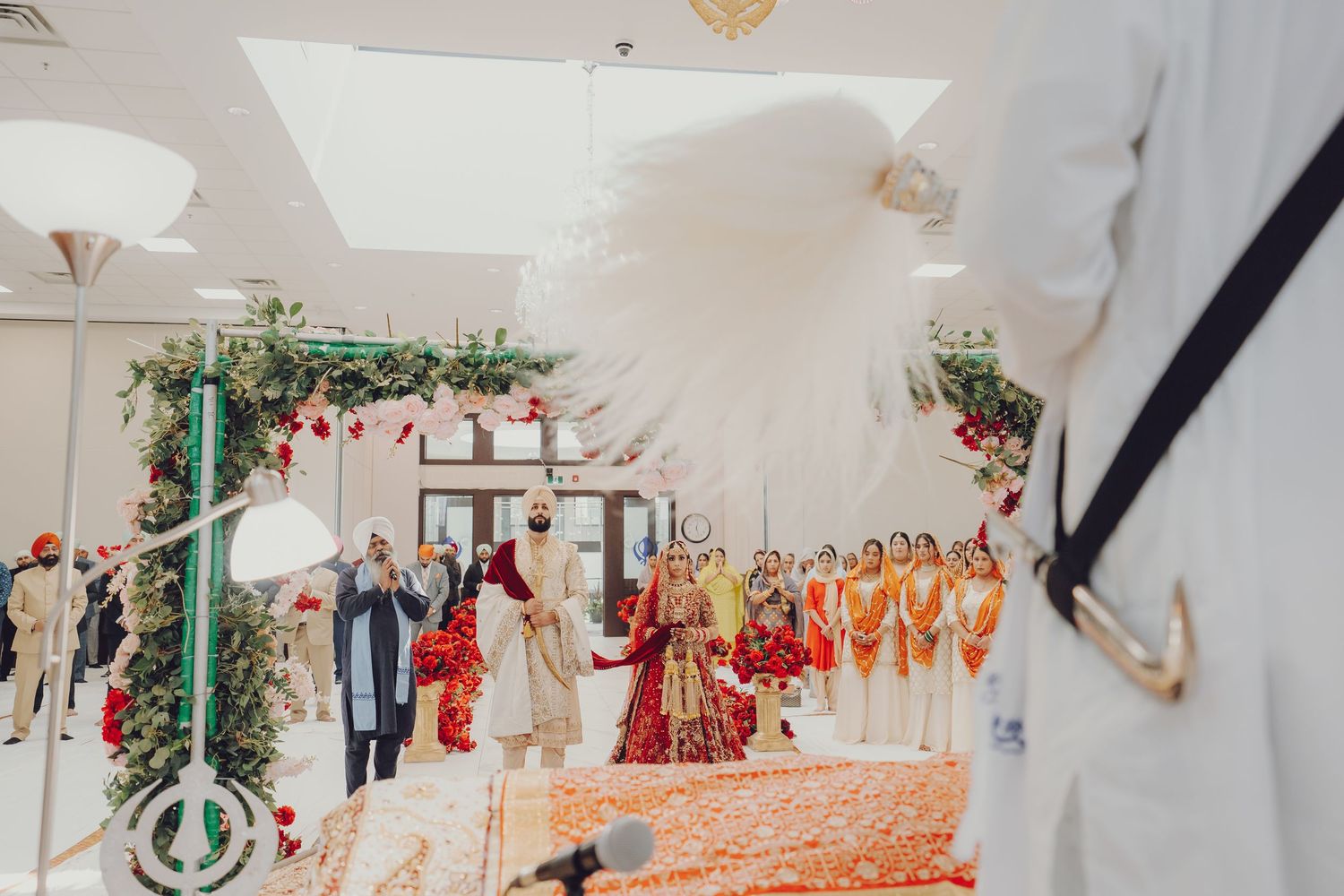 Wedding hall interior featuring ornate decorations with red floral arrangements and white drapery.