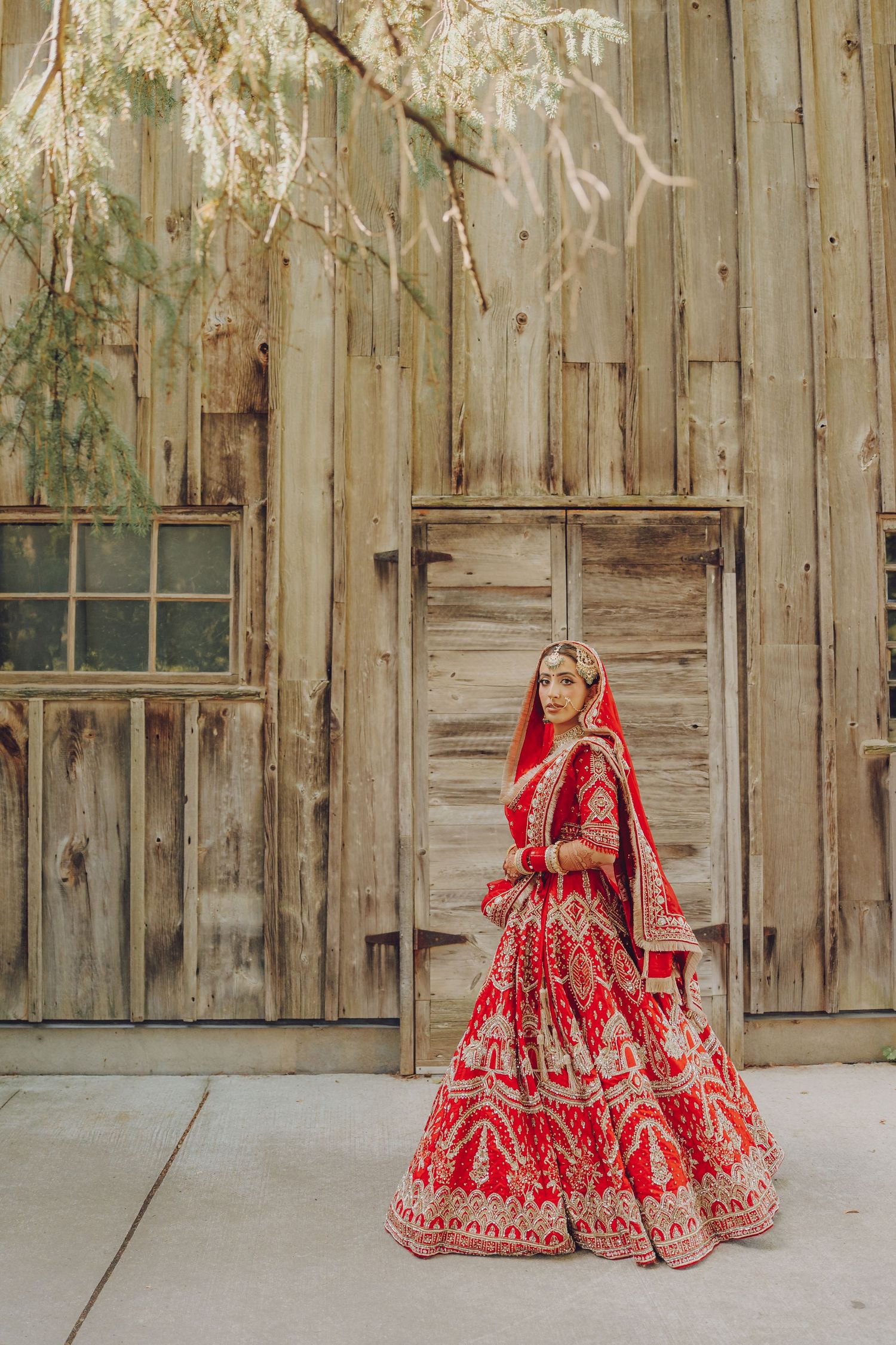 A vibrant red and gold Indian bridal lehenga displayed against a rustic wooden wall backdrop.
