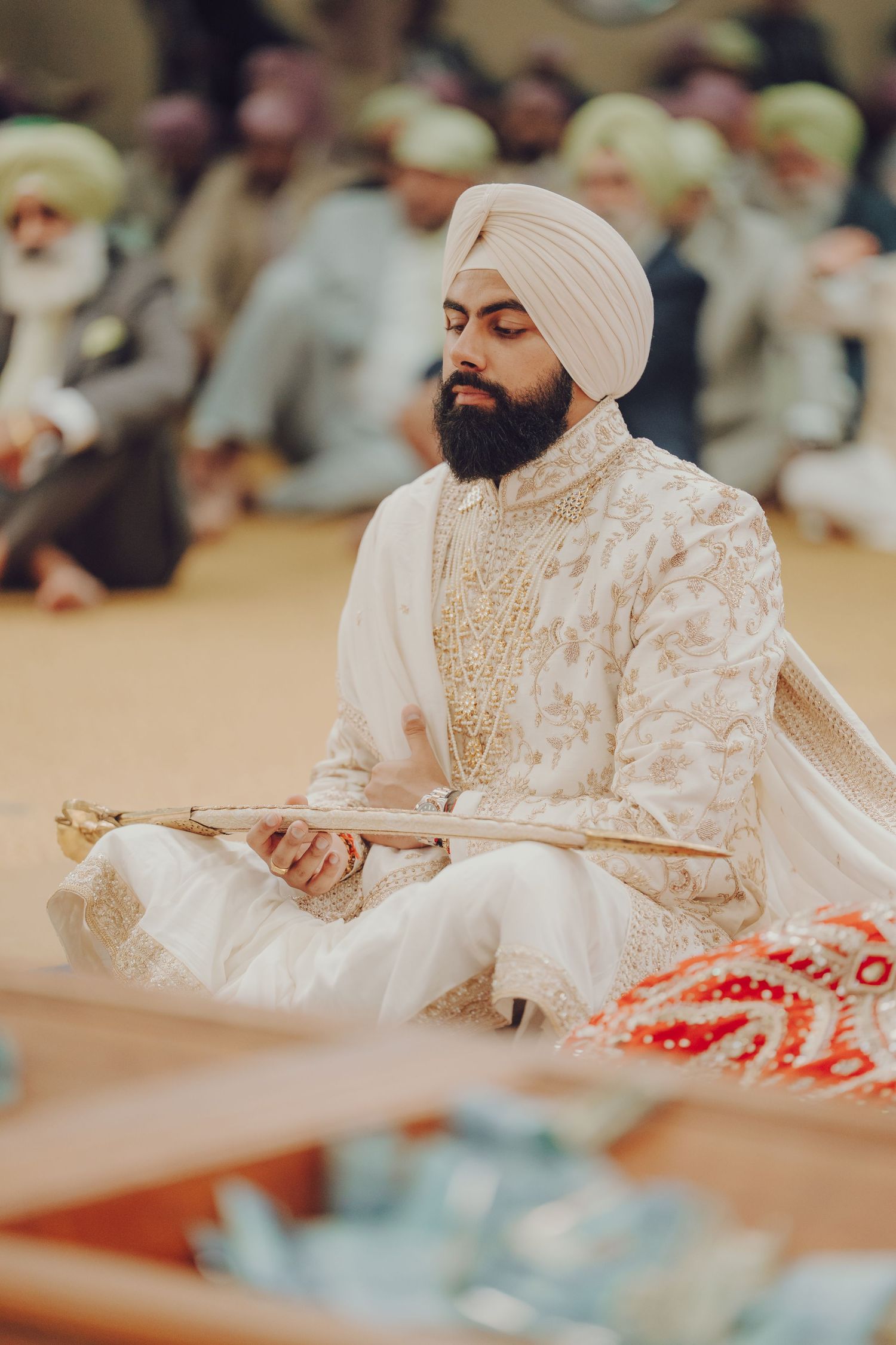 Sikh groom in traditional white attire seated during religious wedding ceremony.