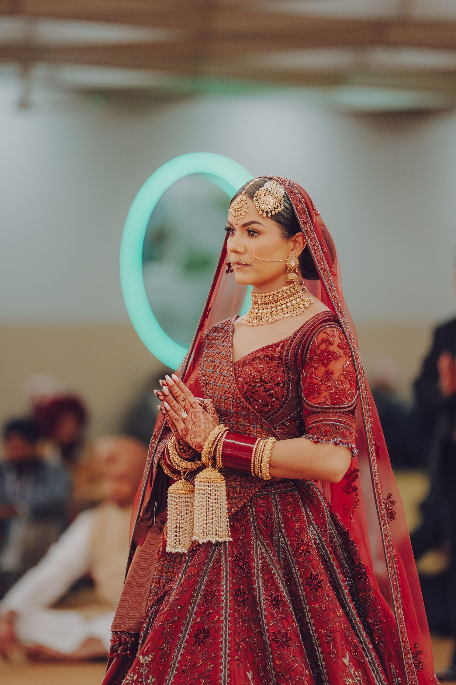 Bride in burgundy lehenga with gold jewelry performing traditional wedding ceremony rituals.