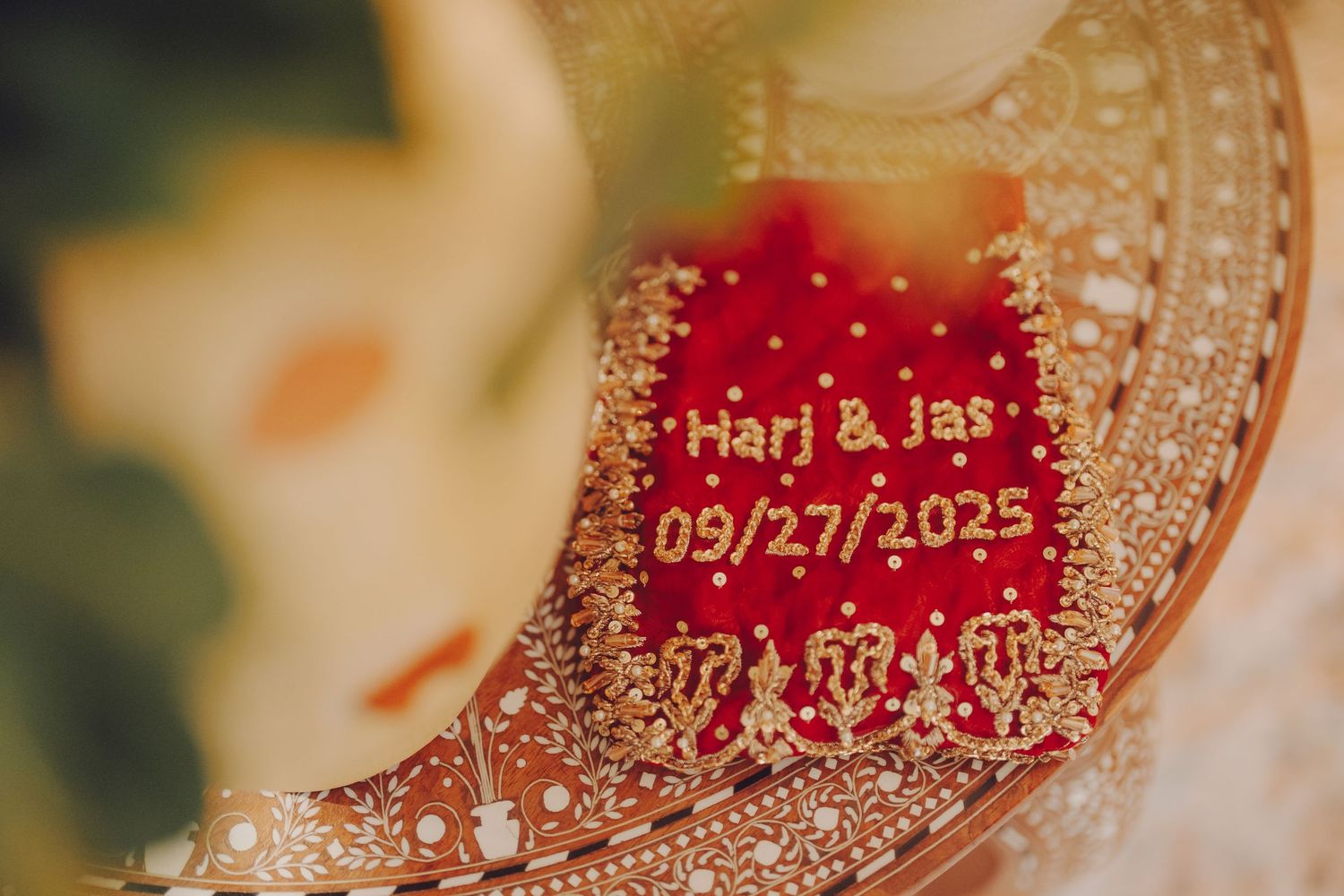A close-up of embroidered wedding details showing names and date on red fabric with gold embellishments.