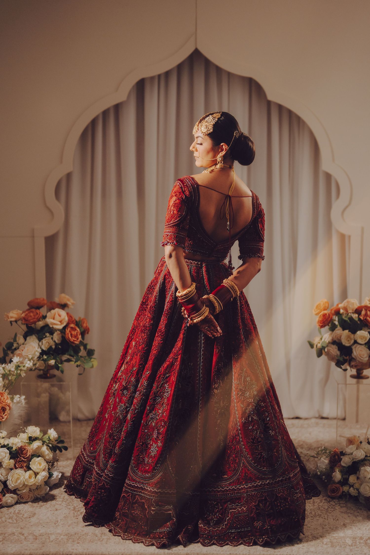 Elegant red and gold embroidered lehenga captured in a traditional Indian wedding setting with floral decor.