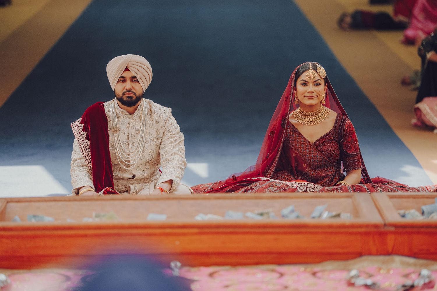 Sikh wedding ceremony in progress with attendees seated on floor in traditional religious setting.