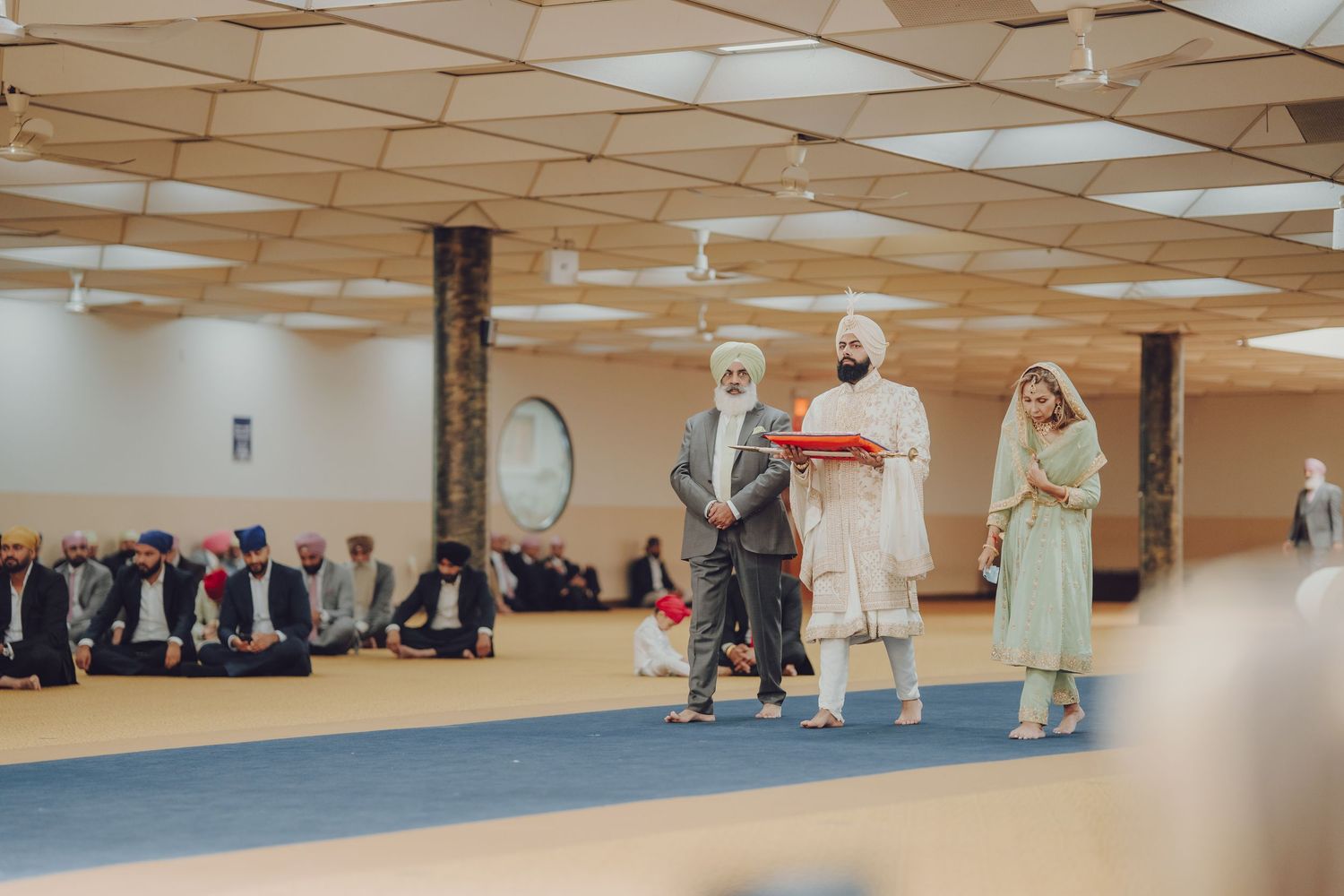 Wide view of a Sikh temple interior with people seated on the floor during ceremony.